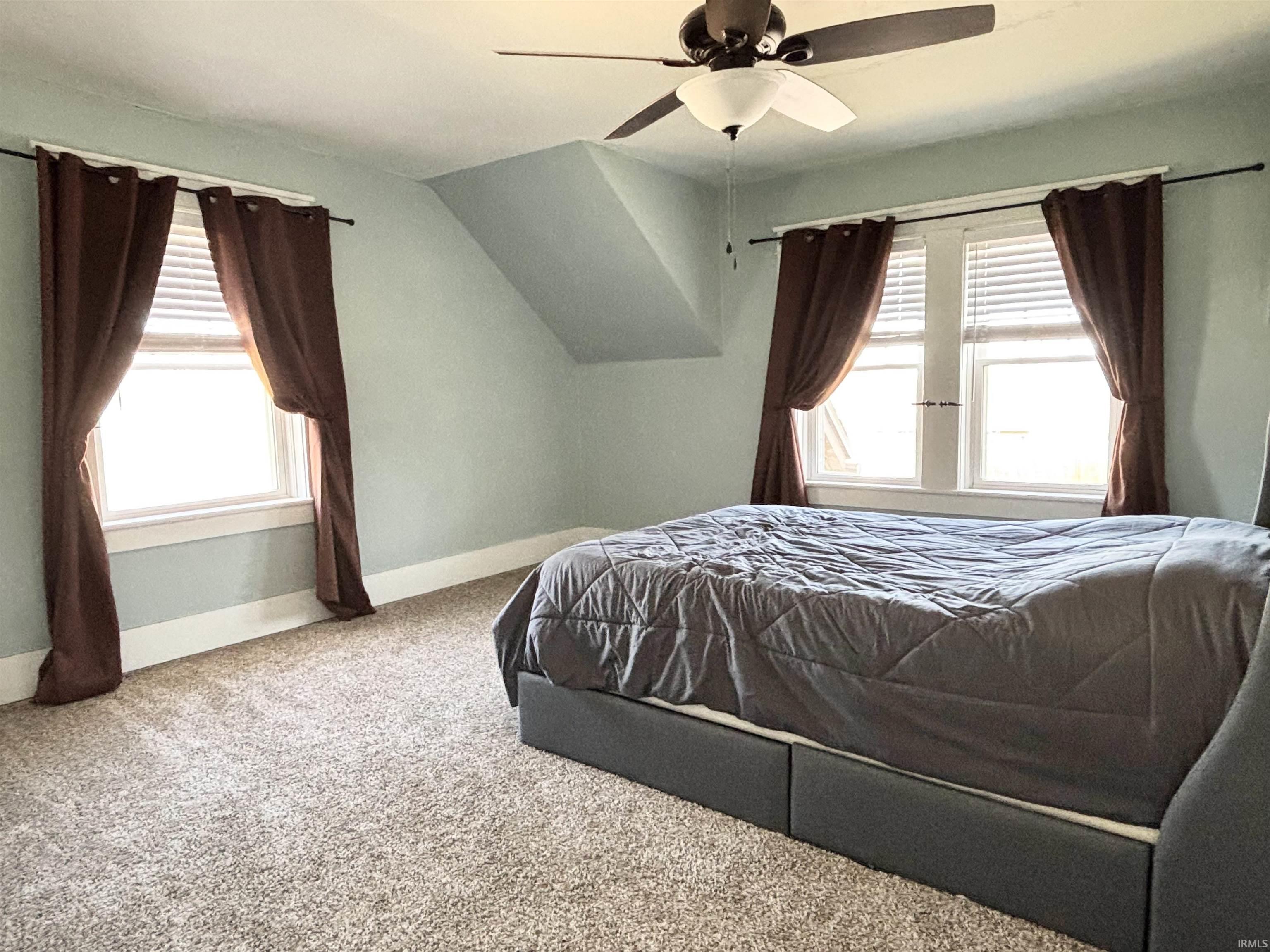 Carpeted bedroom featuring lofted ceiling, multiple windows, and a ceiling fan