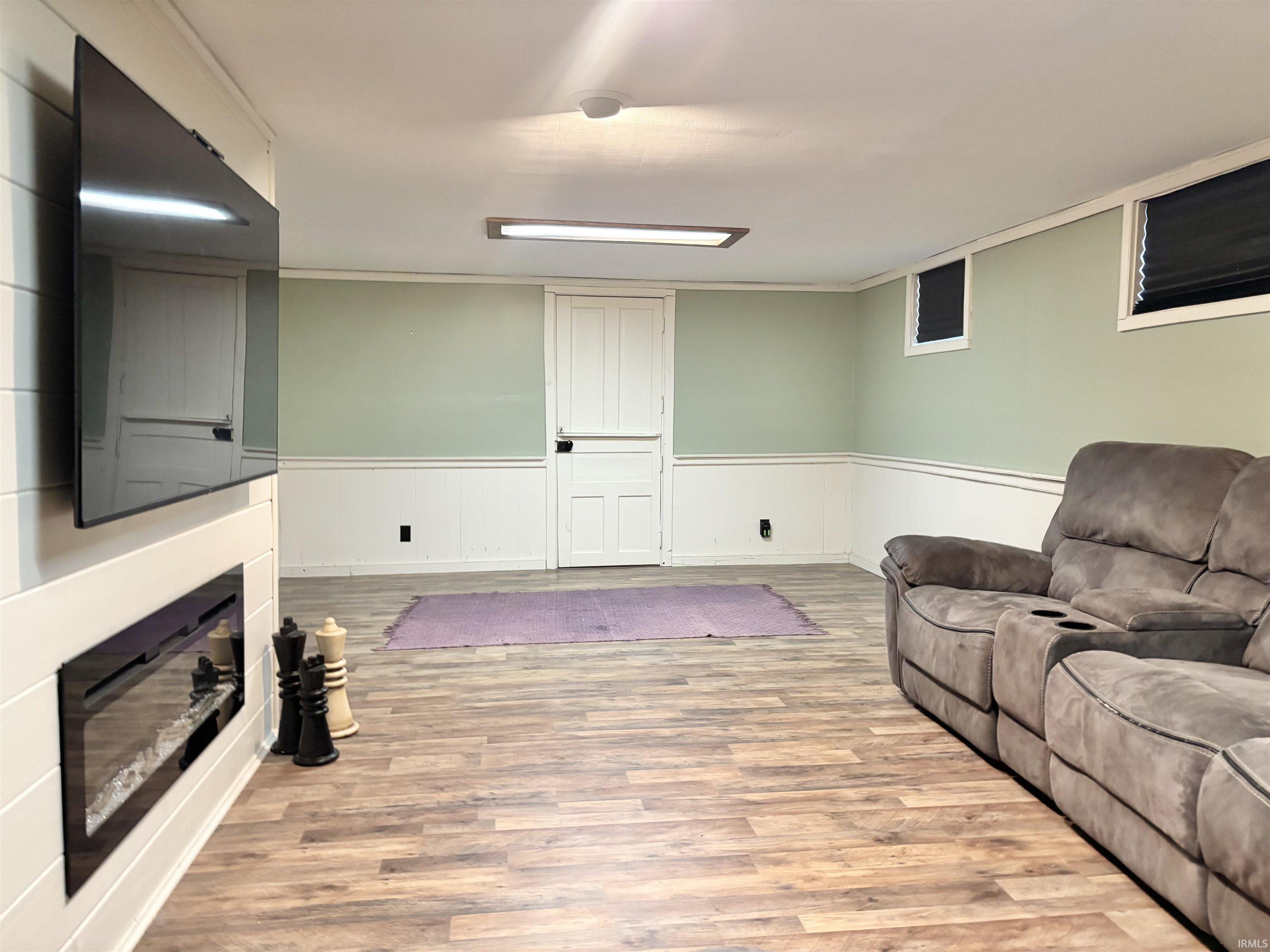 Living area featuring light wood-style floors, a glass covered fireplace, and a wainscoted wall