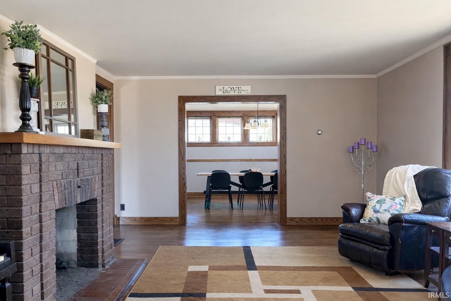 Living room with wood finished floors, crown molding, and a brick fireplace