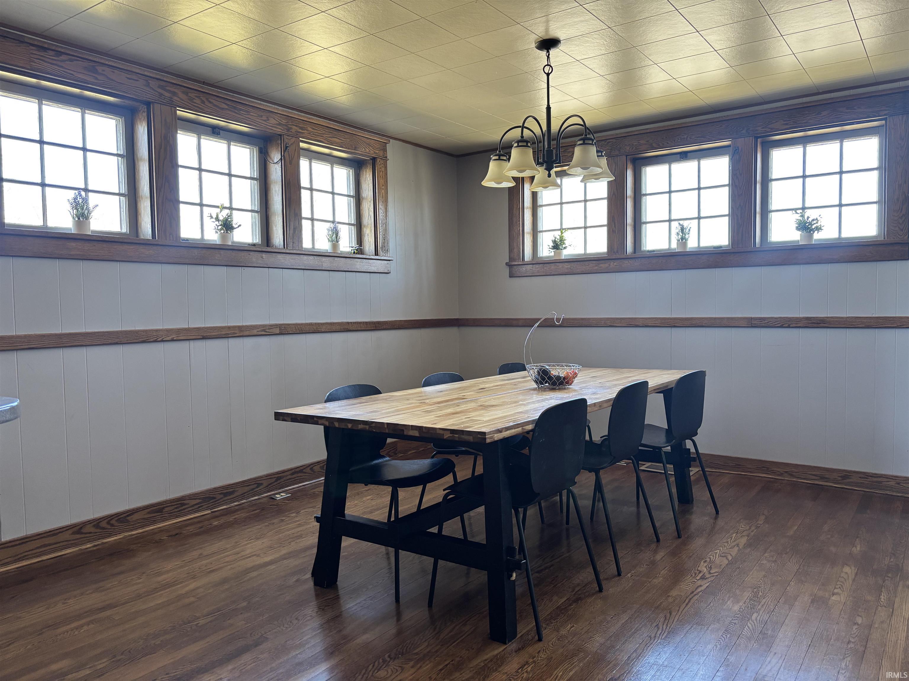Dining room featuring wood walls, dark wood-style flooring, and hanging lights
