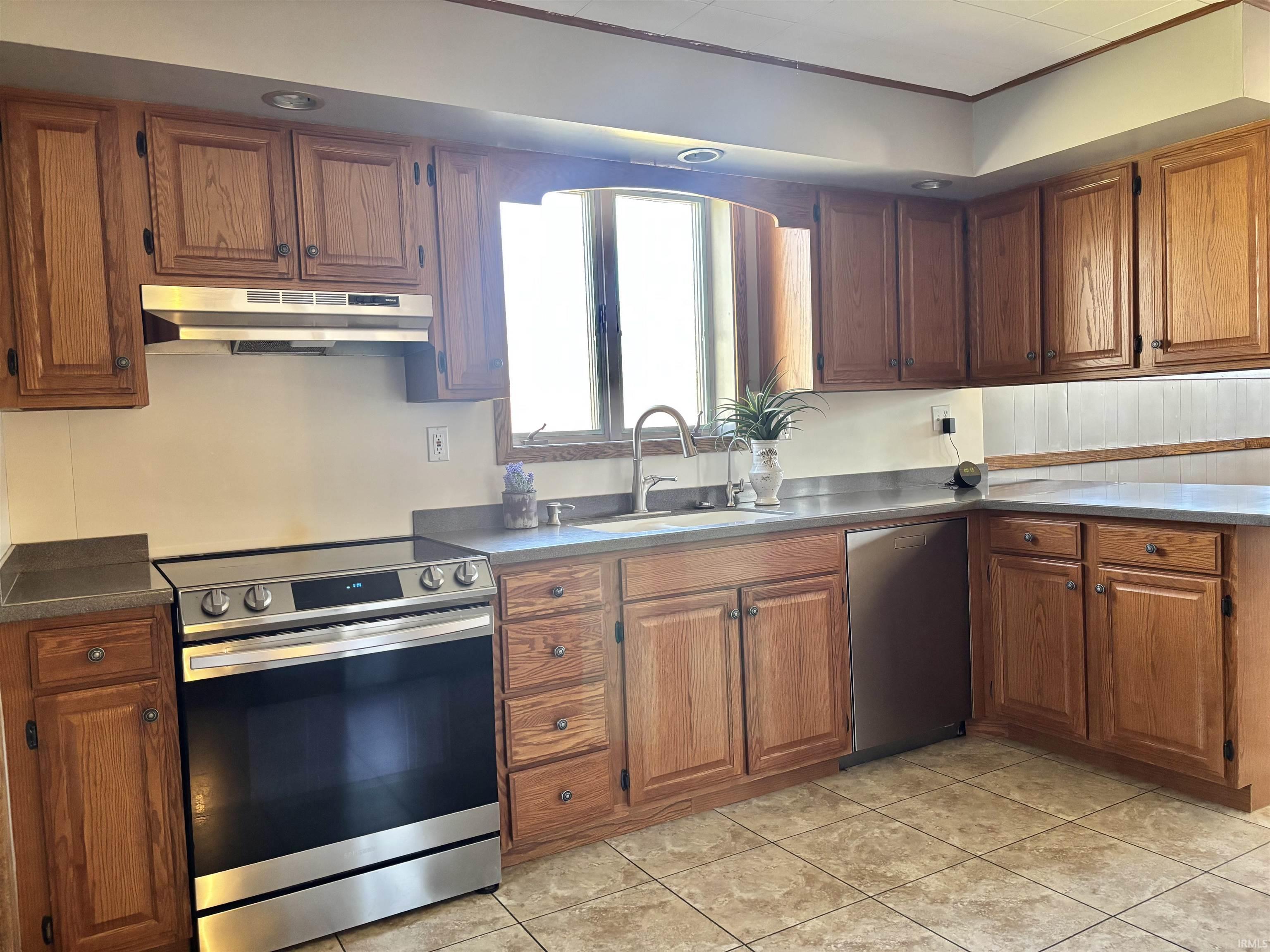 Kitchen with stainless steel appliances, wood finish cabinetry, light tile patterned floors, and dark countertops