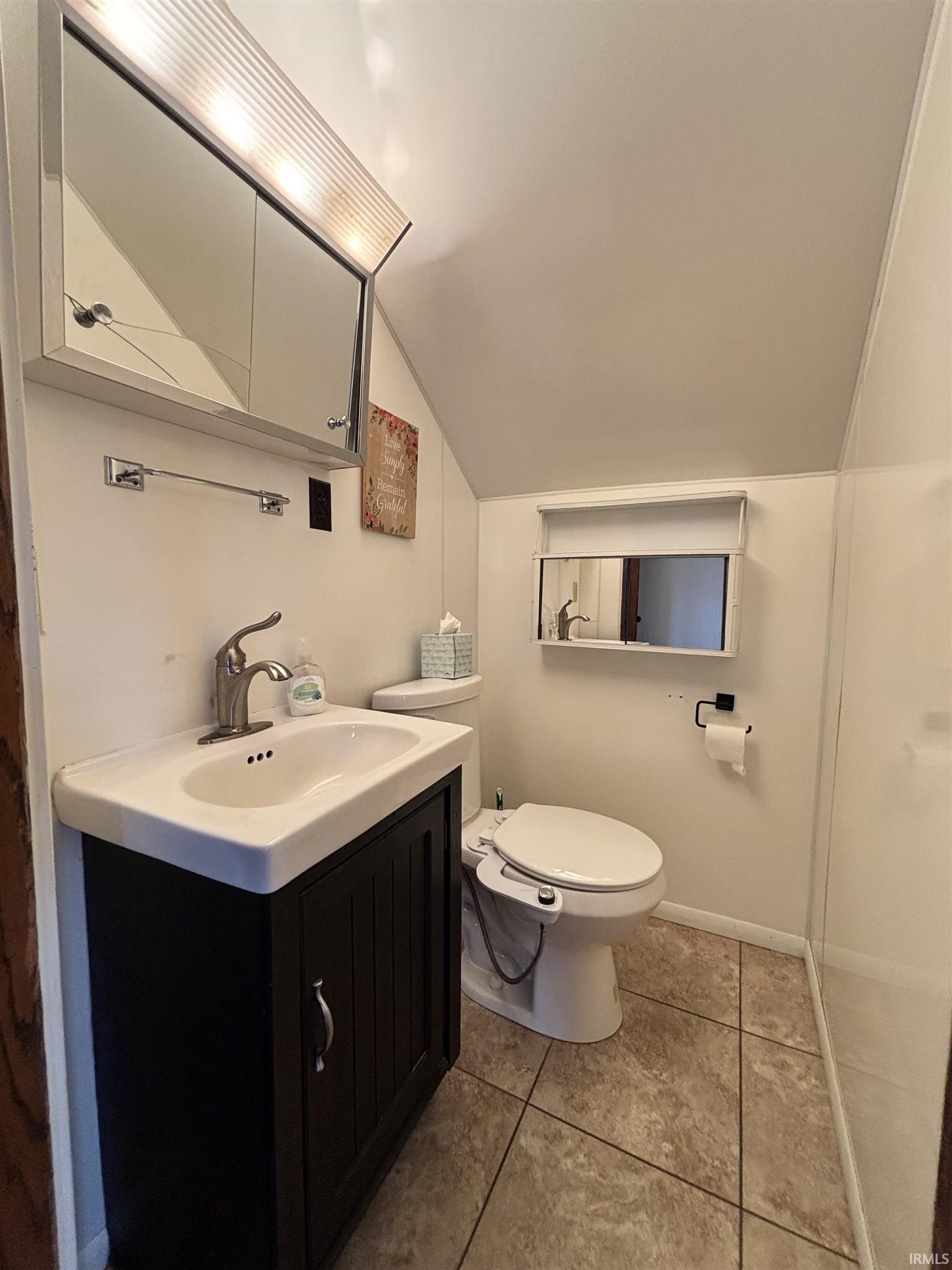 Half bathroom featuring vanity, vaulted ceiling, and light tile patterned floors