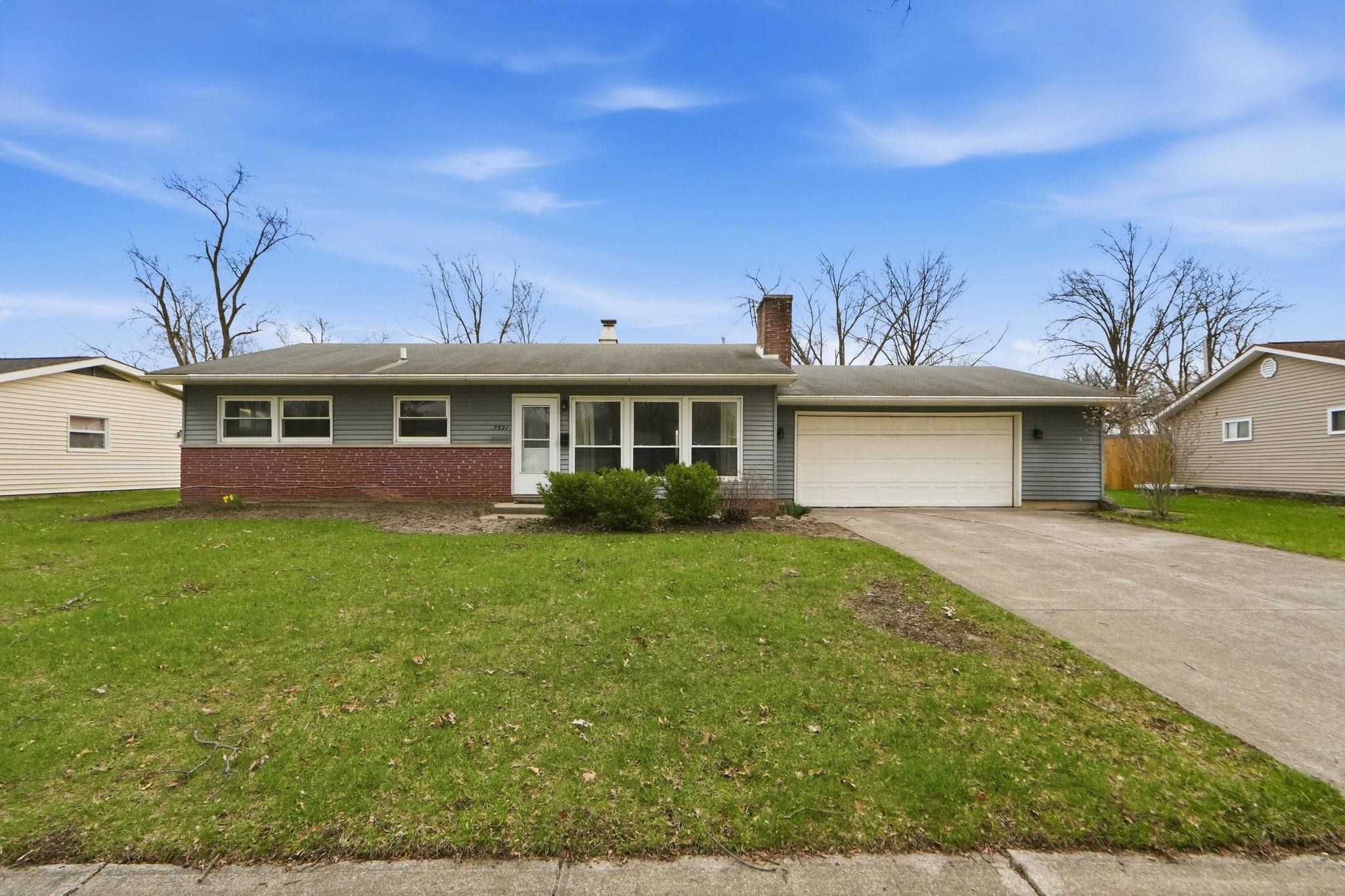 Ranch-style house with a chimney, an attached garage, concrete driveway, brick siding, and a front yard