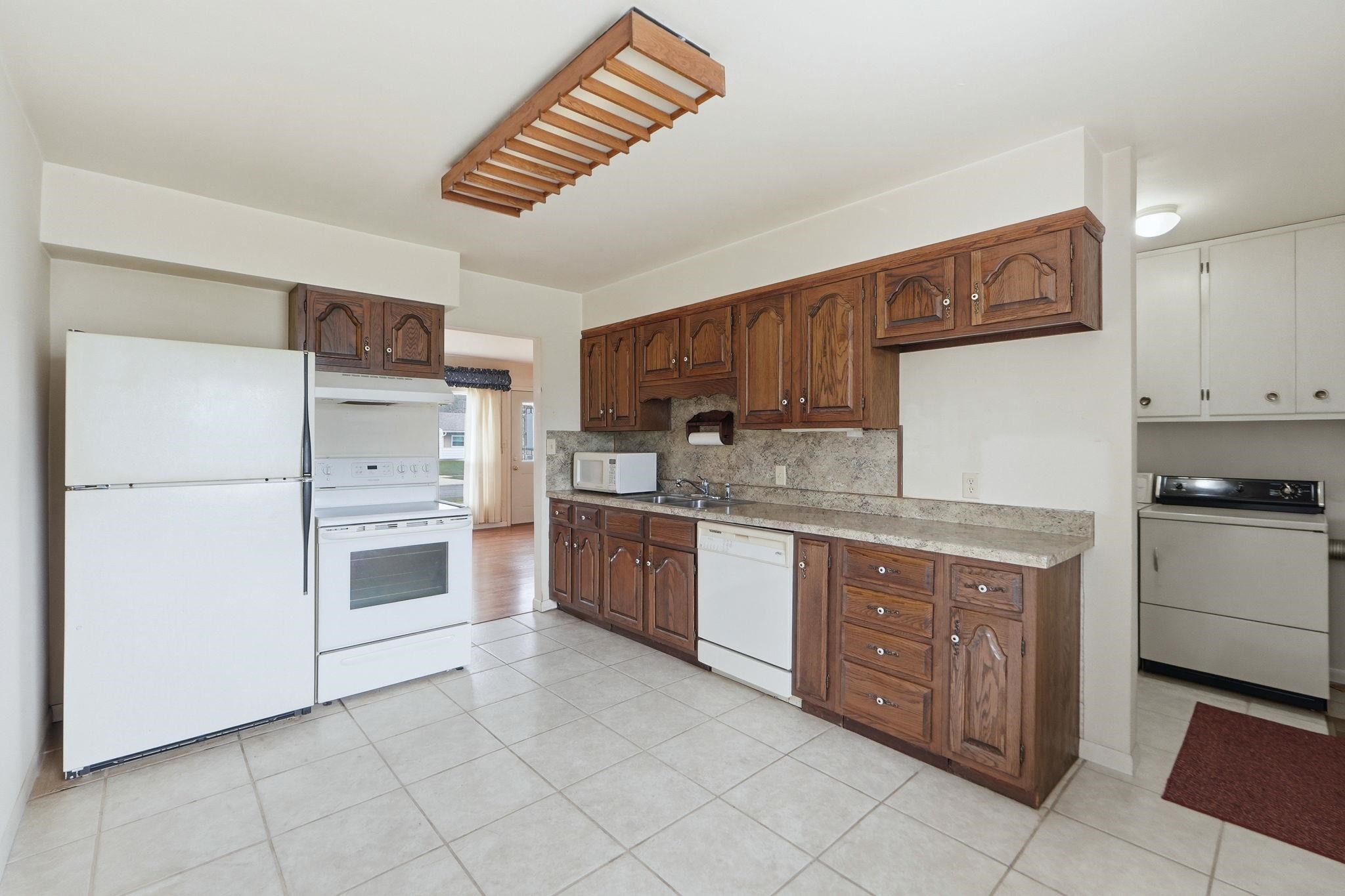 Kitchen with white appliances, light countertops, washer / clothes dryer, light tile patterned floors, and backsplash