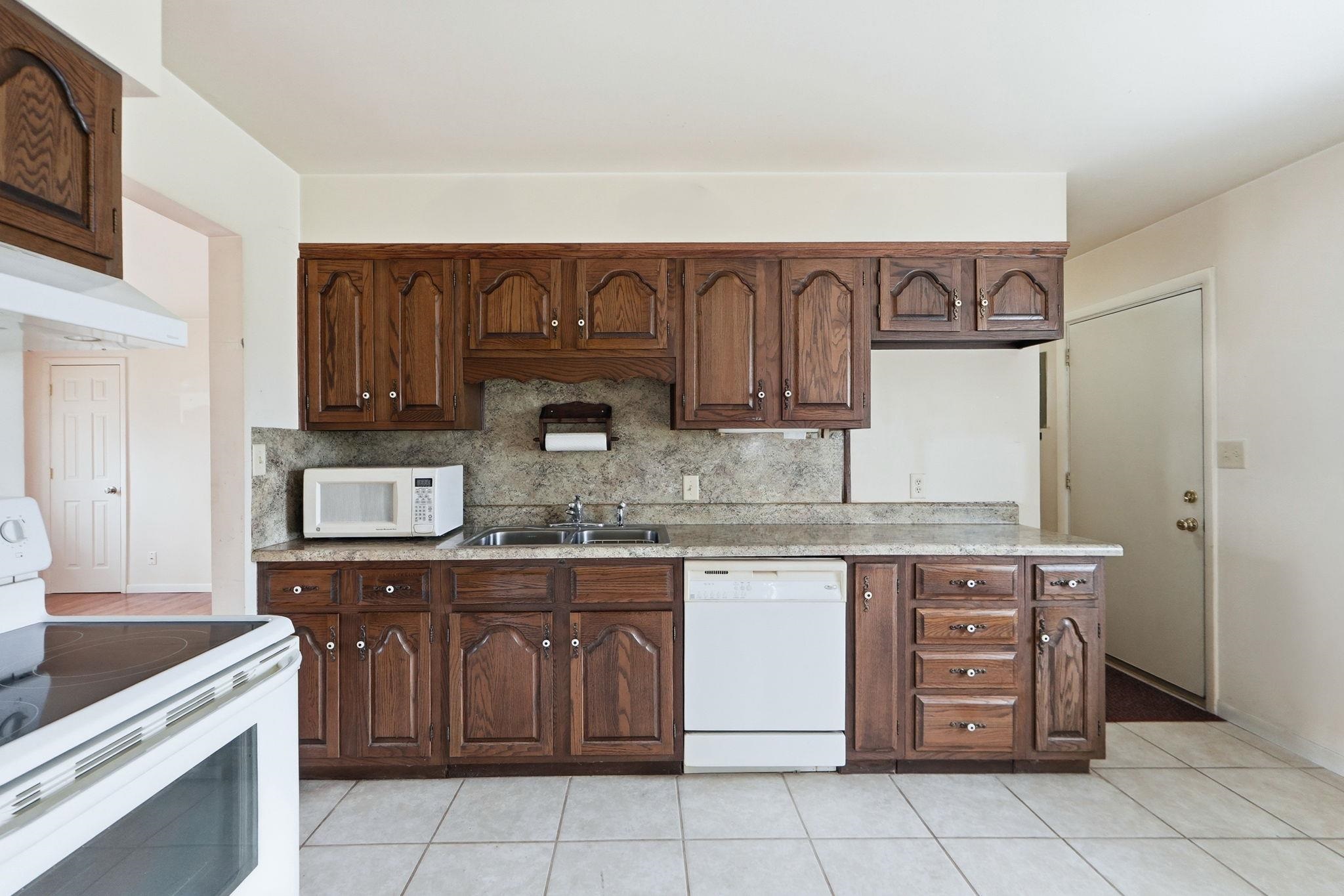 Kitchen featuring white appliances, light countertops, tasteful backsplash, light tile patterned flooring, and dark wood finish cabinetry