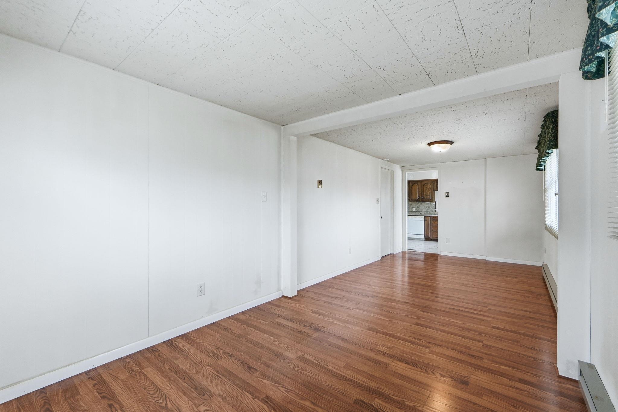 Empty room featuring dark wood-type flooring and a baseboard heating unit