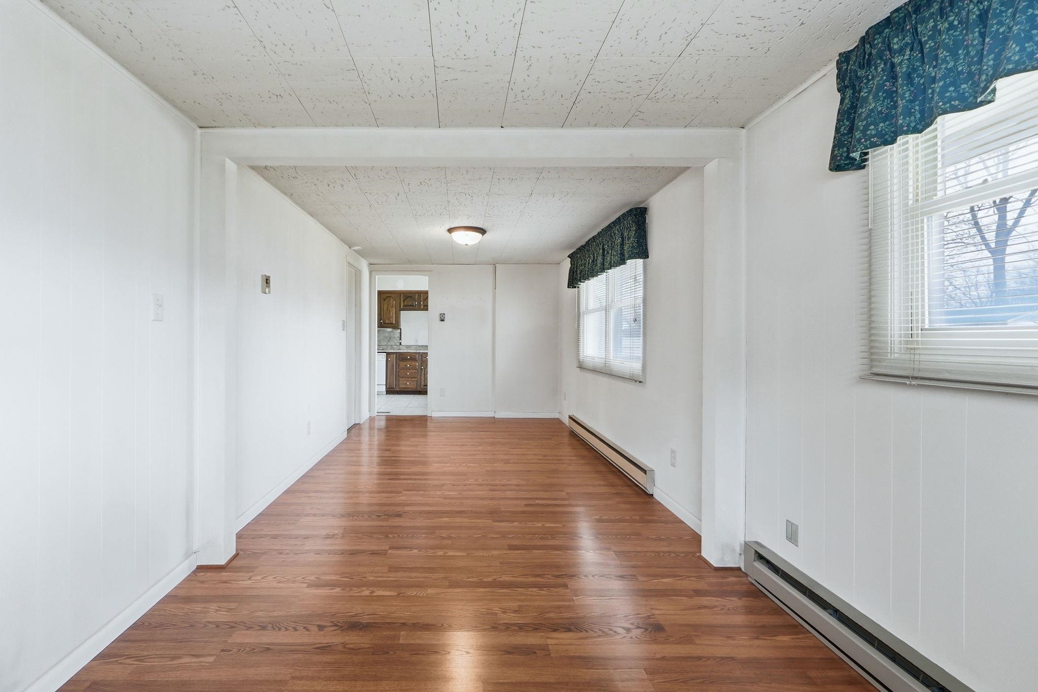 Unfurnished living room featuring baseboard heating and dark wood-style floors
