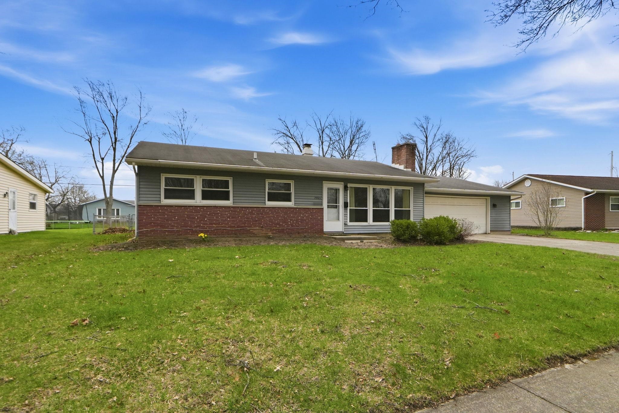 Single story home with a chimney, brick siding, a garage, a front lawn, and concrete driveway