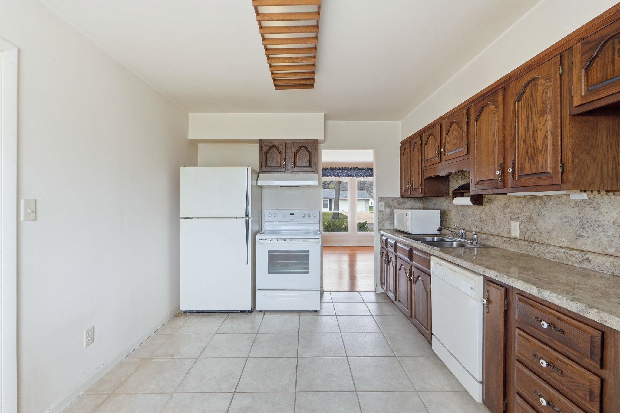 Kitchen with light countertops, white appliances, light tile patterned floors, tasteful backsplash, and wood finish cabinetry