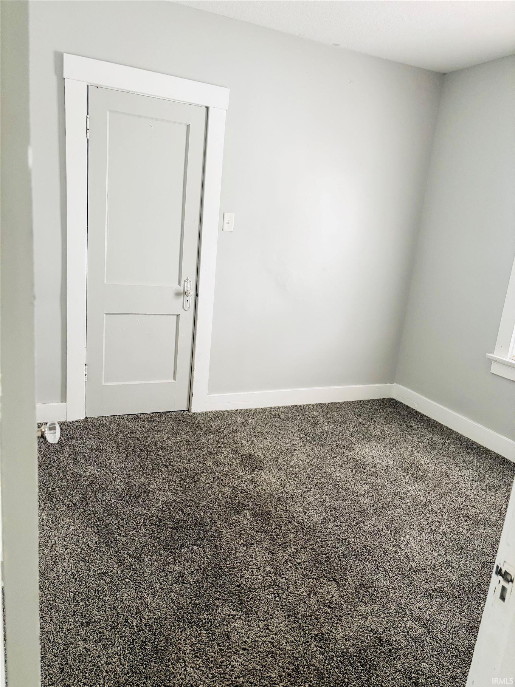 Unfurnished room with dark colored carpet and baseboards