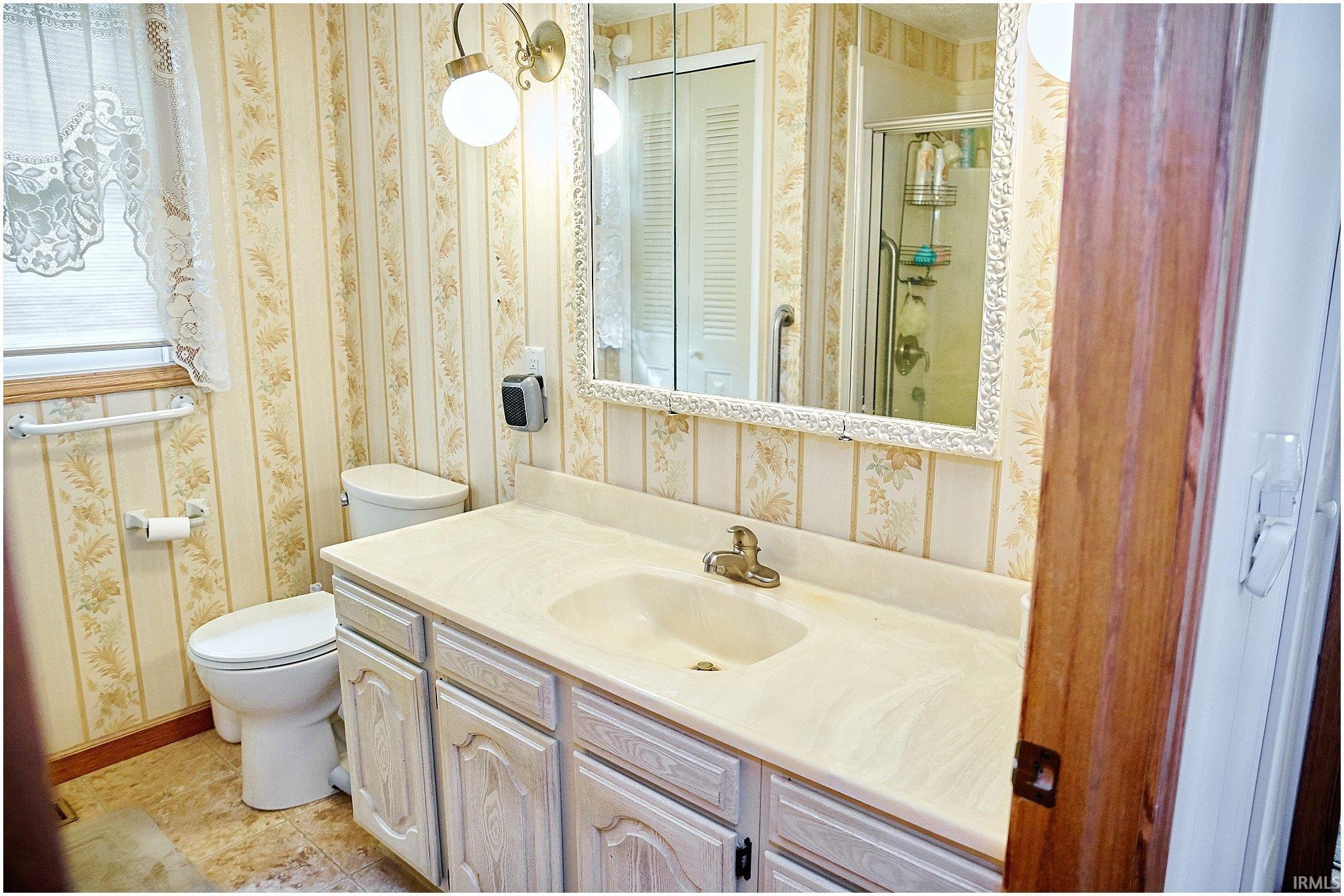 Bathroom with a stall shower, vanity, wallpapered walls, and light tile patterned floors