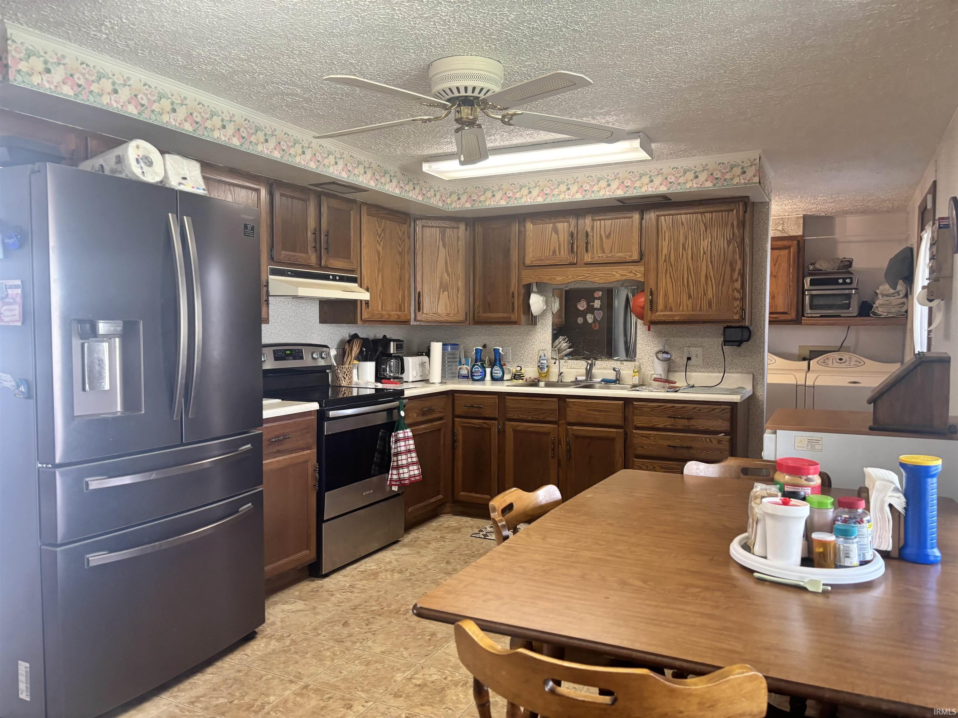 Kitchen featuring stainless steel appliances, ceiling fan, light countertops, a textured ceiling, and dark wood finish cabinetry