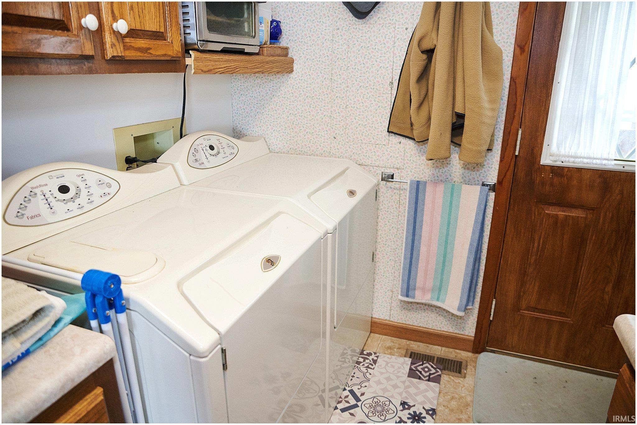 Laundry room featuring wallpapered walls, washing machine and clothes dryer, and cabinet space