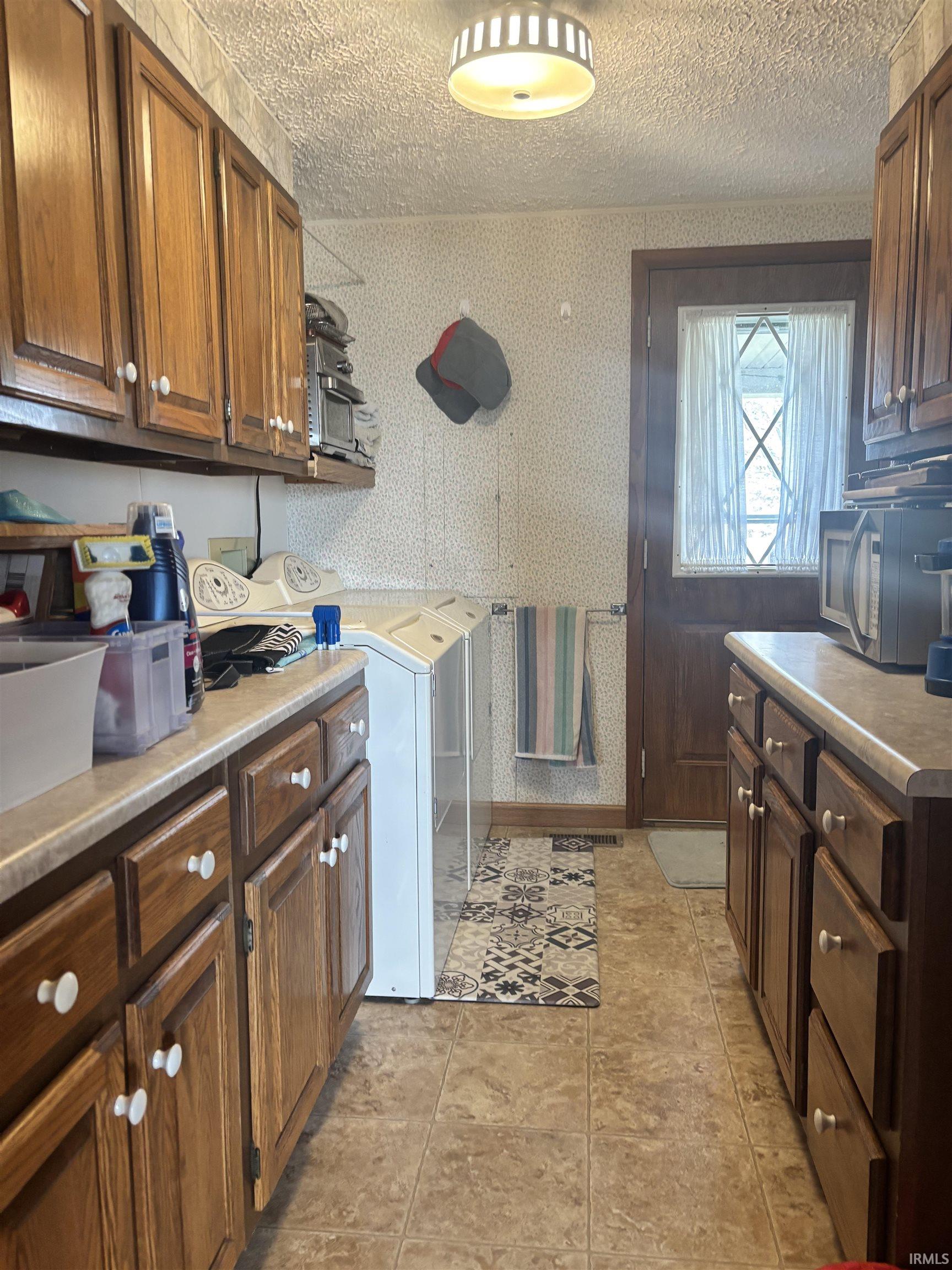 Laundry area featuring wallpapered walls, a textured ceiling, washing machine and clothes dryer, and cabinet space