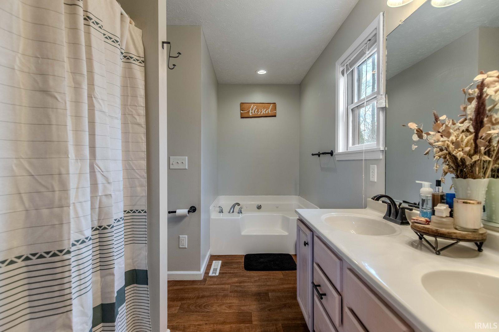 Full bath with double vanity, a garden tub, dark wood finished floors, a shower with curtain, and recessed lighting