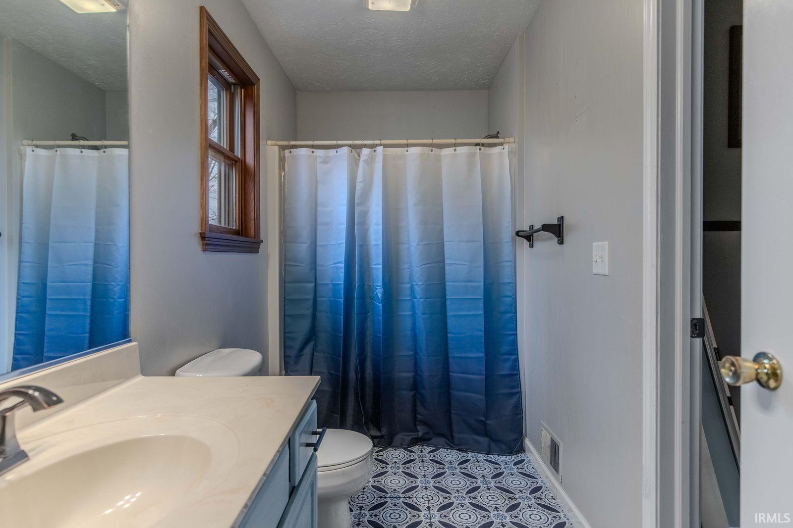 Bathroom with vanity, a shower with shower curtain, a textured ceiling, and light tile patterned floors