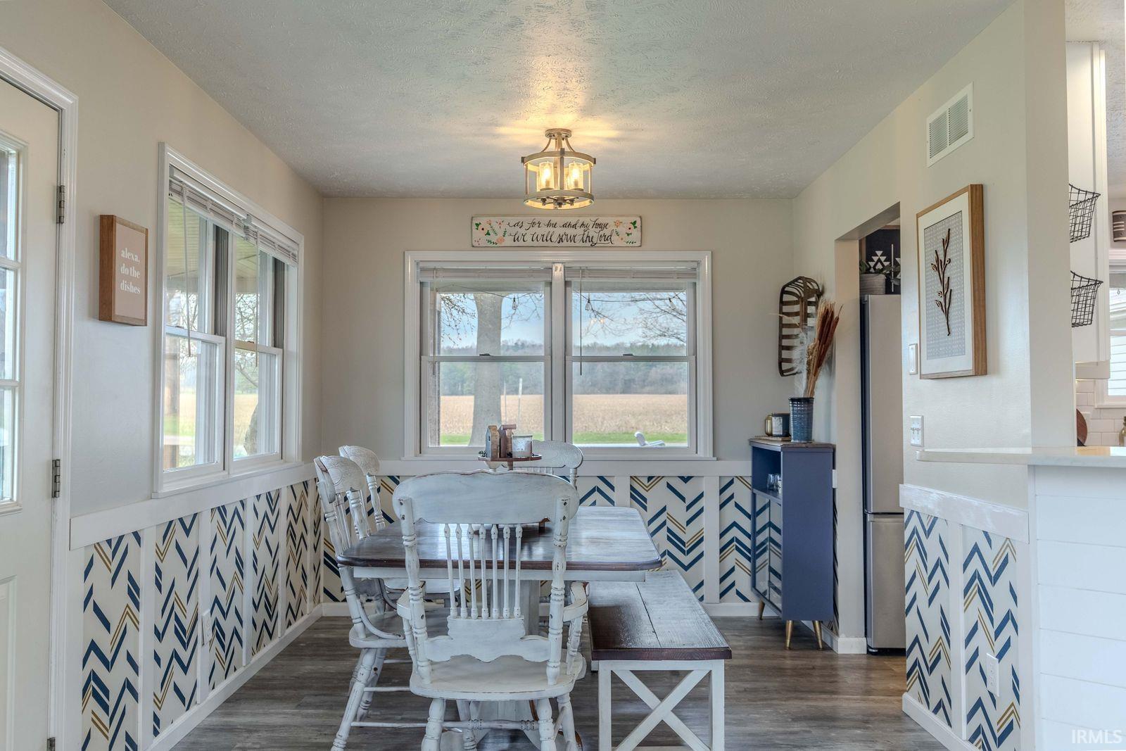 Dining space featuring wainscoting, dark wood finished floors, a textured ceiling, plenty of natural light, and wallpapered walls