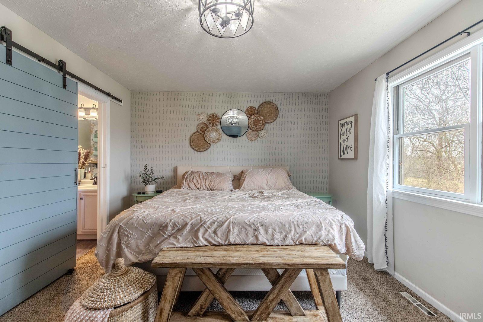 Bedroom featuring a barn door, carpet flooring, connected bathroom, and wallpapered walls