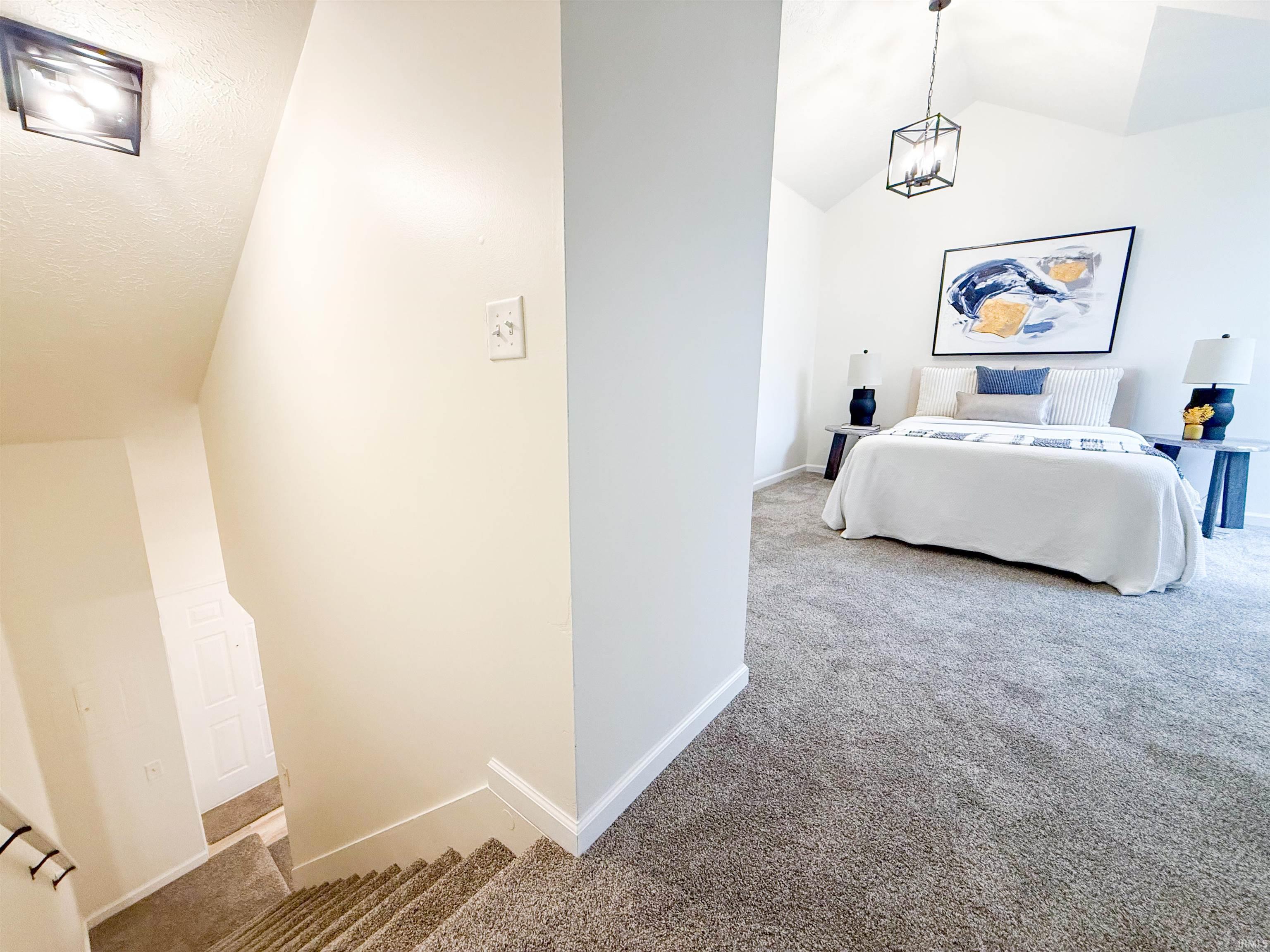 Bedroom with light carpet, vaulted ceiling, and suspended lighting