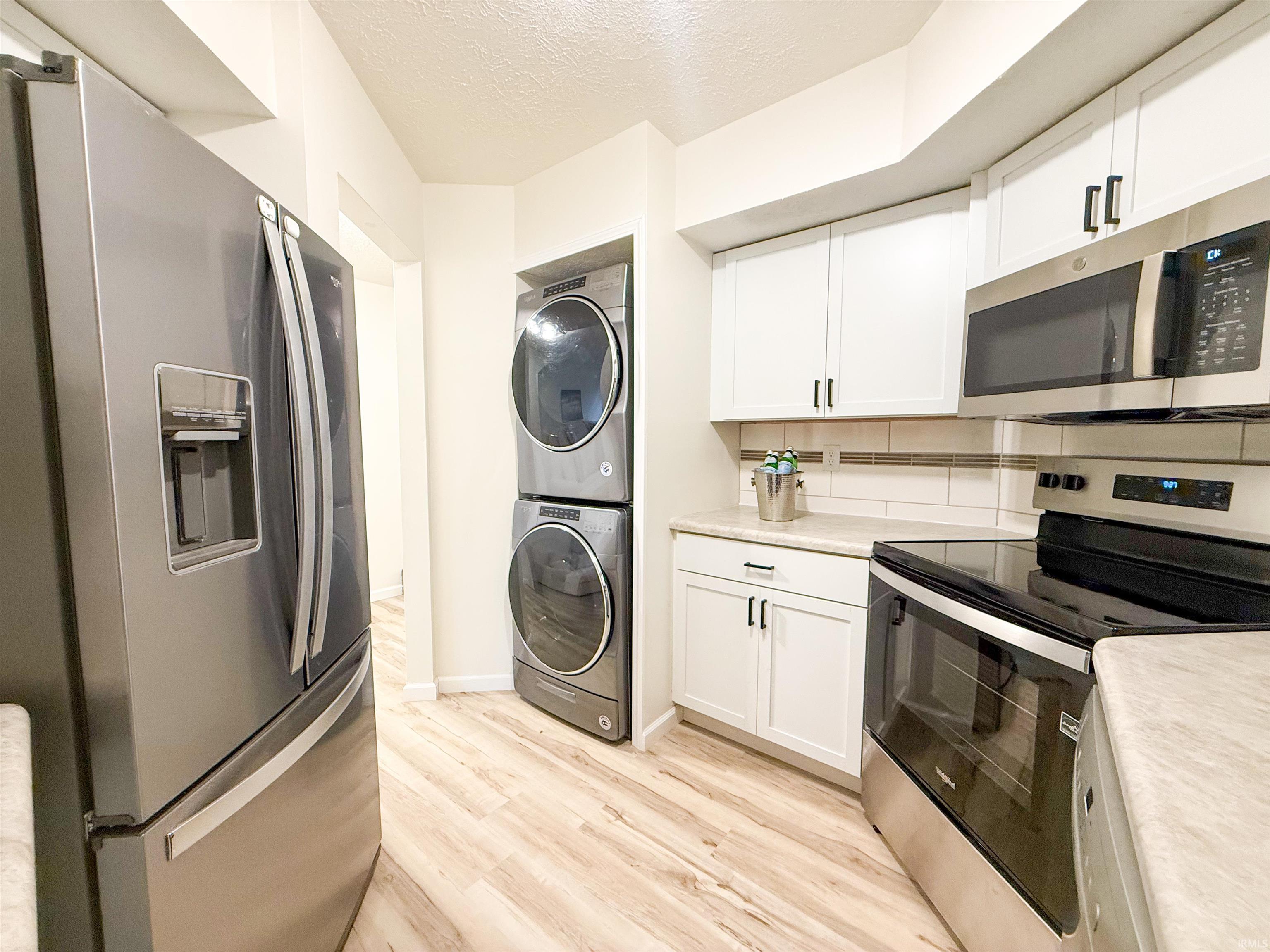 Kitchen featuring stainless steel appliances, light countertops, light wood-style flooring, stacked washer / dryer, and a textured ceiling