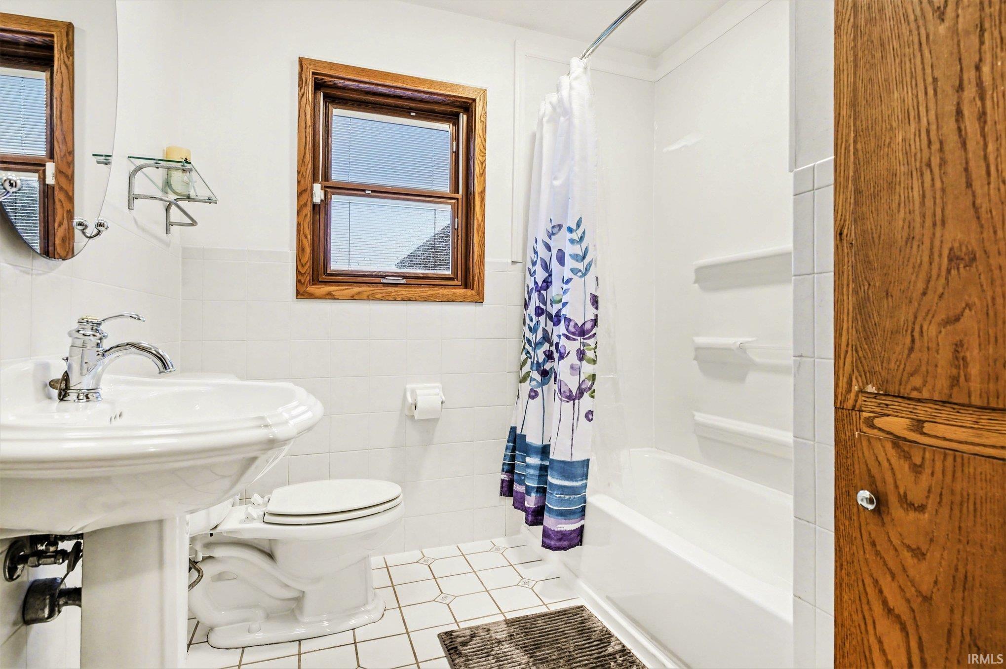 Bathroom featuring light tile patterned floors, tile walls, shower / bath combination with curtain, and wainscoting