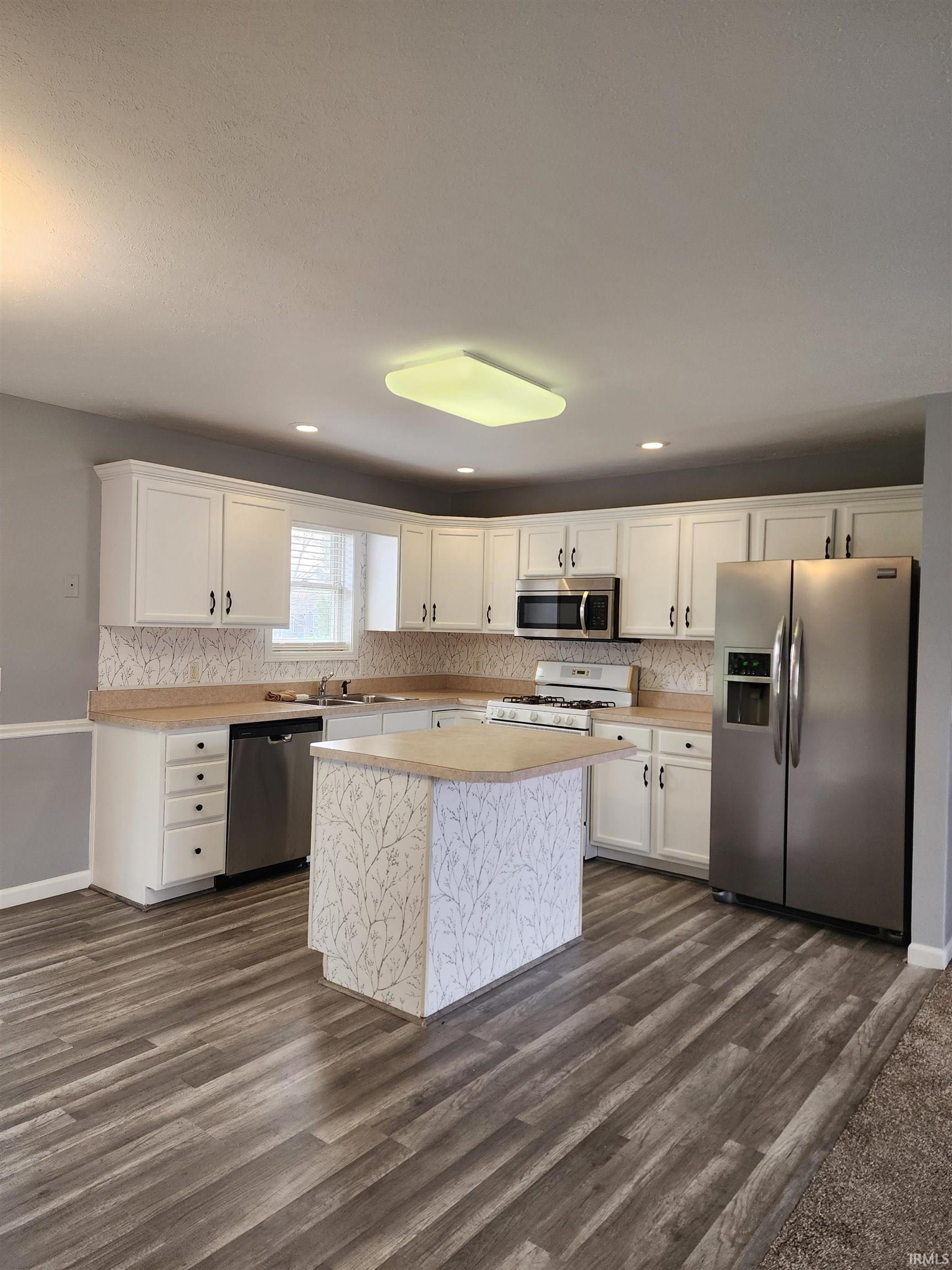 Kitchen with stainless steel appliances, light countertops, white cabinetry, tasteful backsplash, and dark wood-style flooring