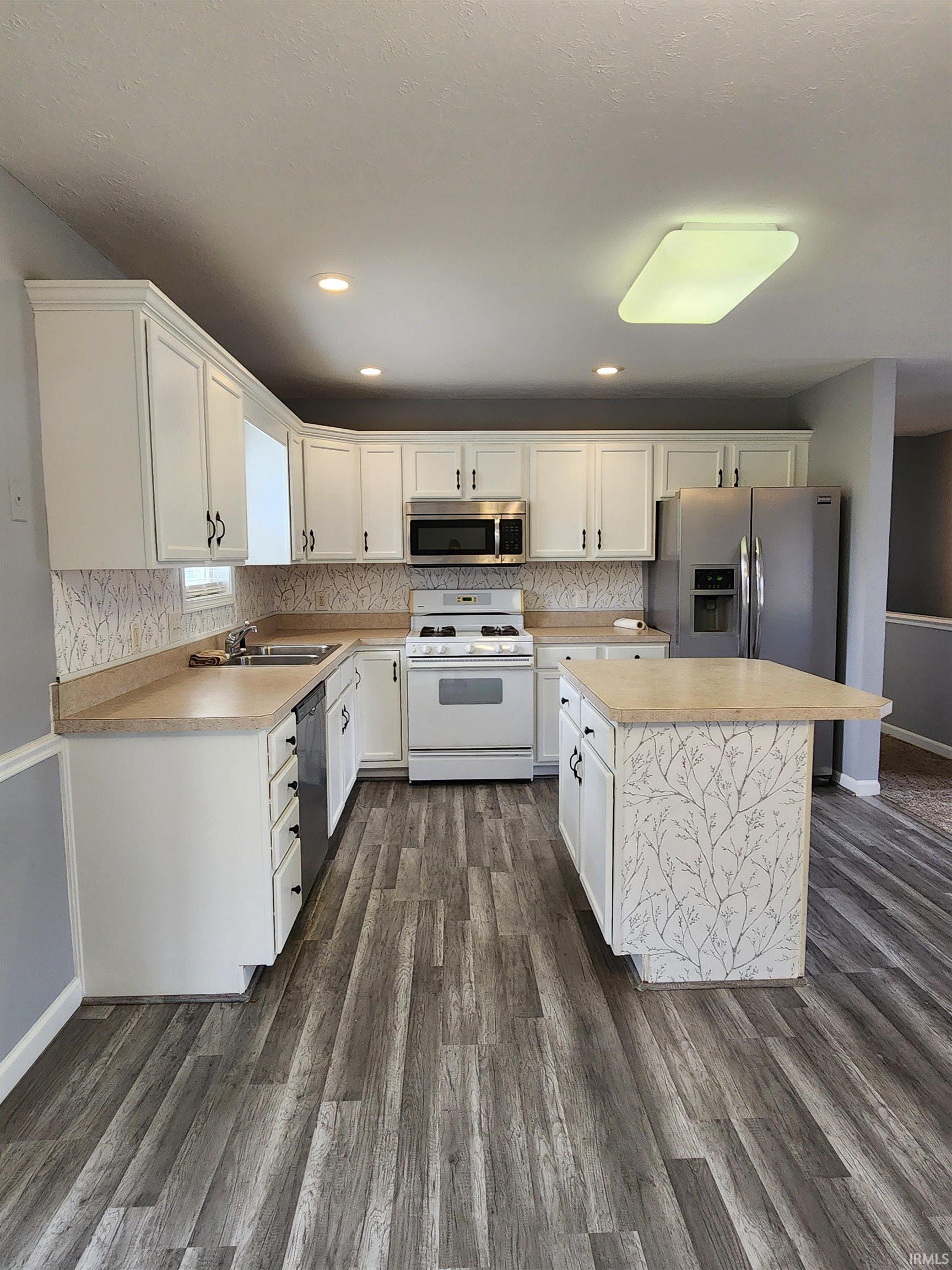 Kitchen featuring stainless steel appliances, light countertops, white cabinetry, a center island, and recessed lighting
