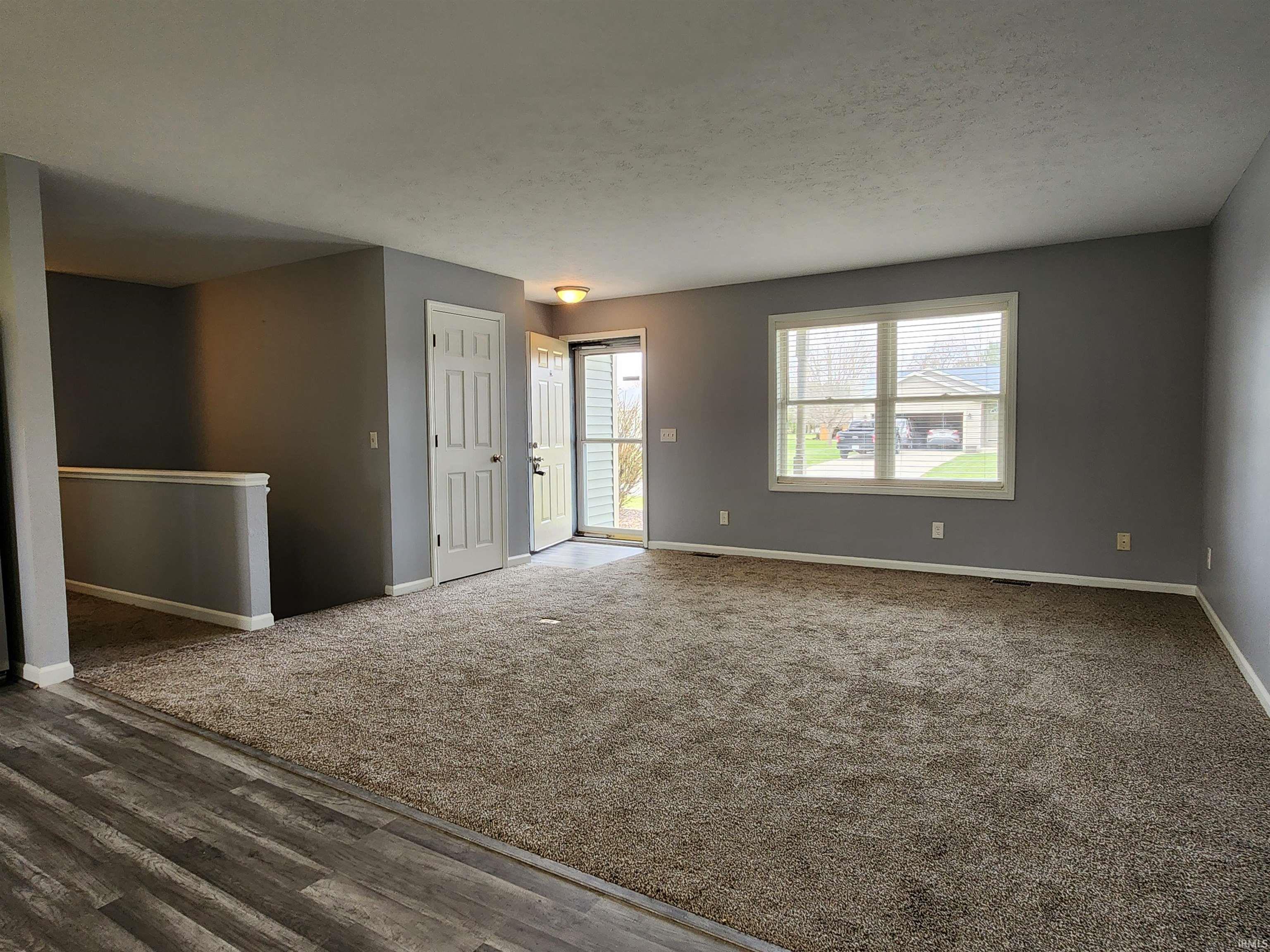 Empty room with dark carpet, dark wood-style flooring, and a textured ceiling