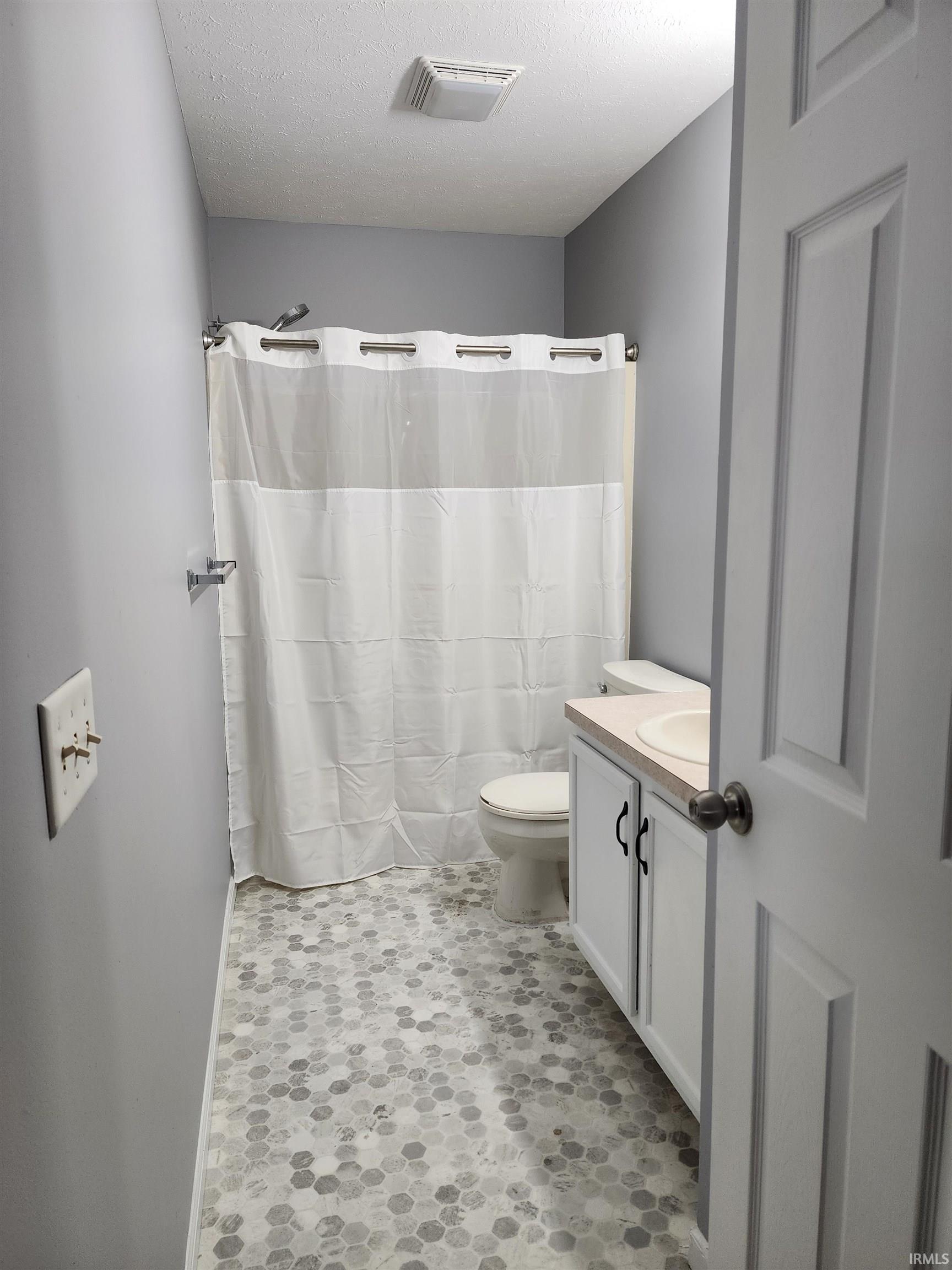 Full bathroom with vanity, a shower with curtain, a textured ceiling, and light flooring