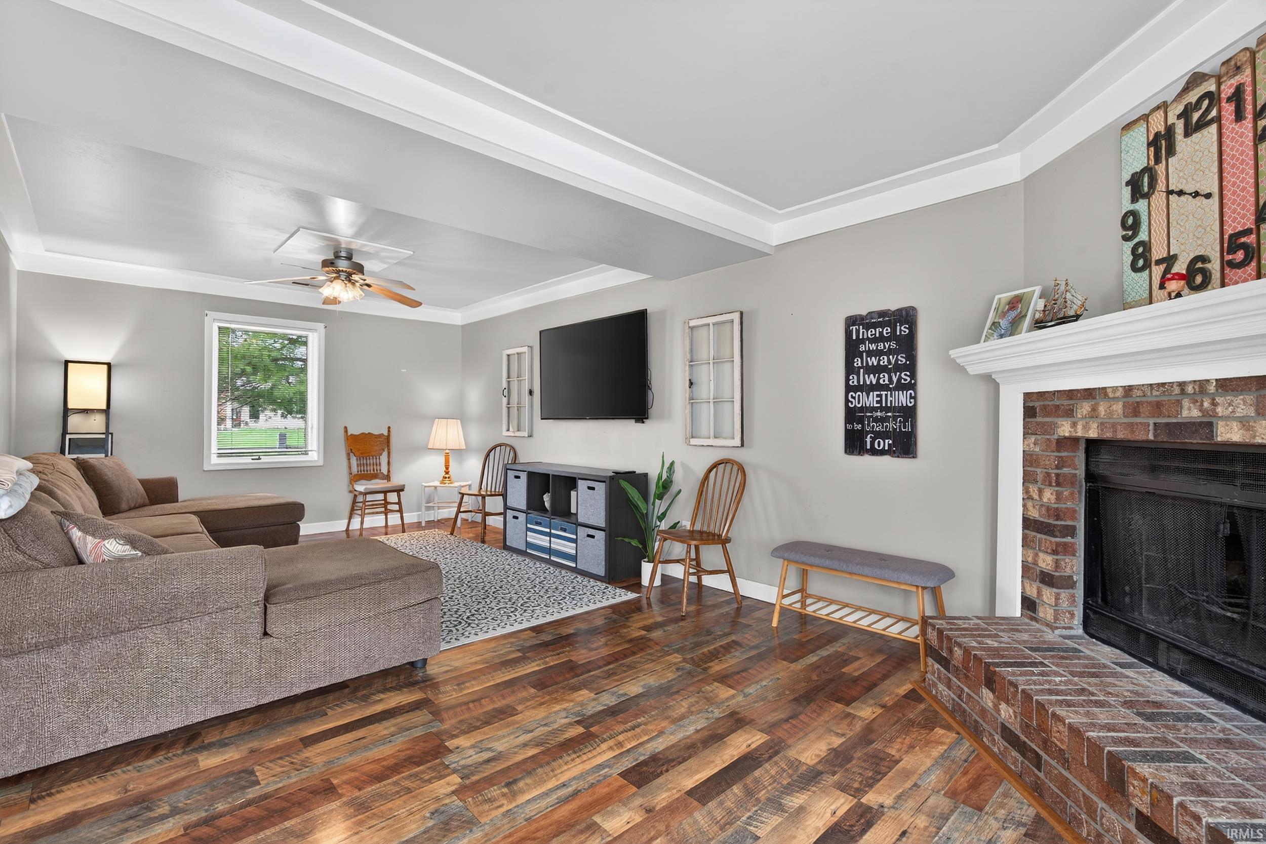 Living area with wood finished floors, a ceiling fan, a fireplace, and ornamental molding