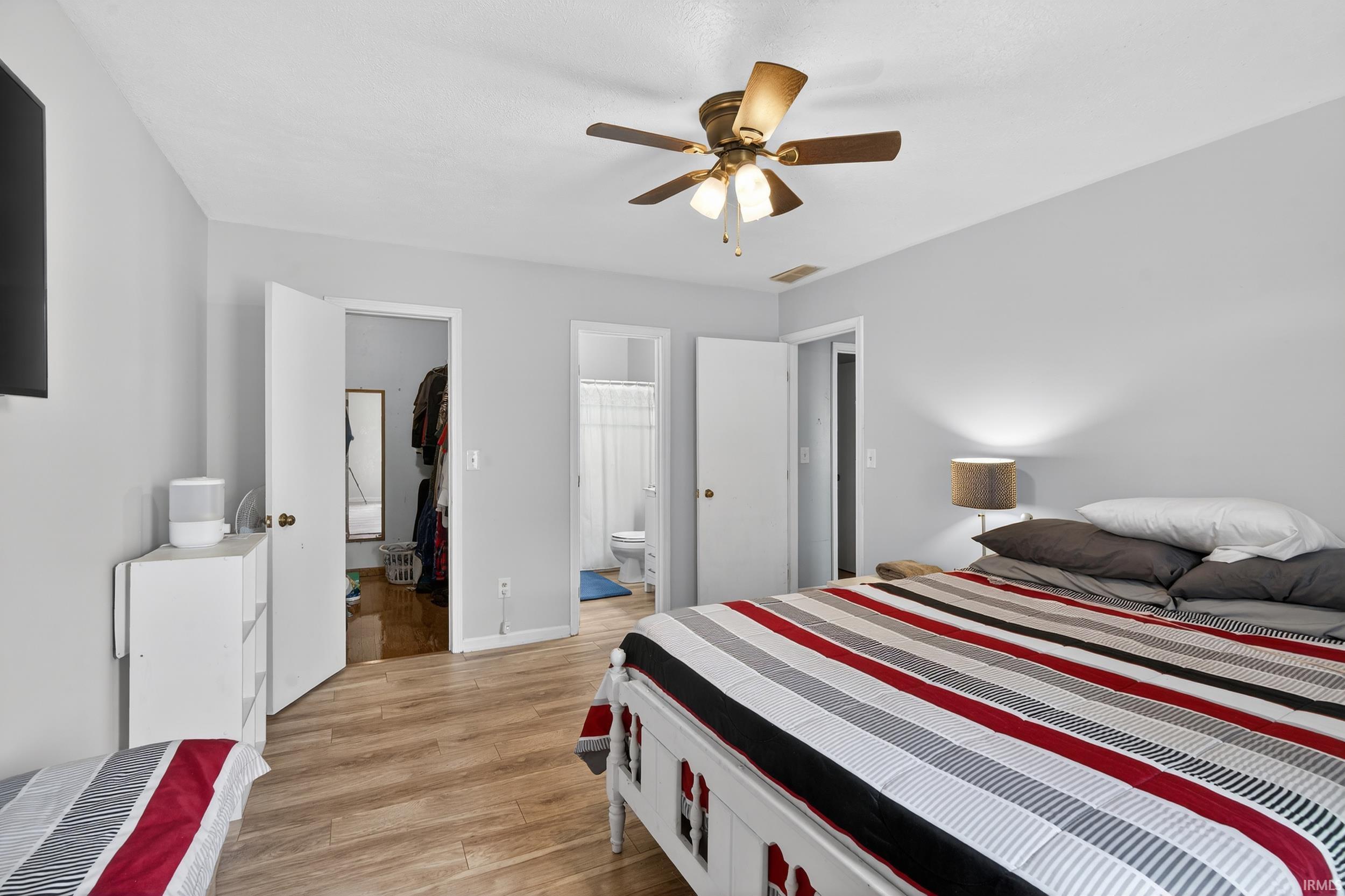 Bedroom with a spacious closet, light wood-type flooring, ensuite bathroom, and a ceiling fan