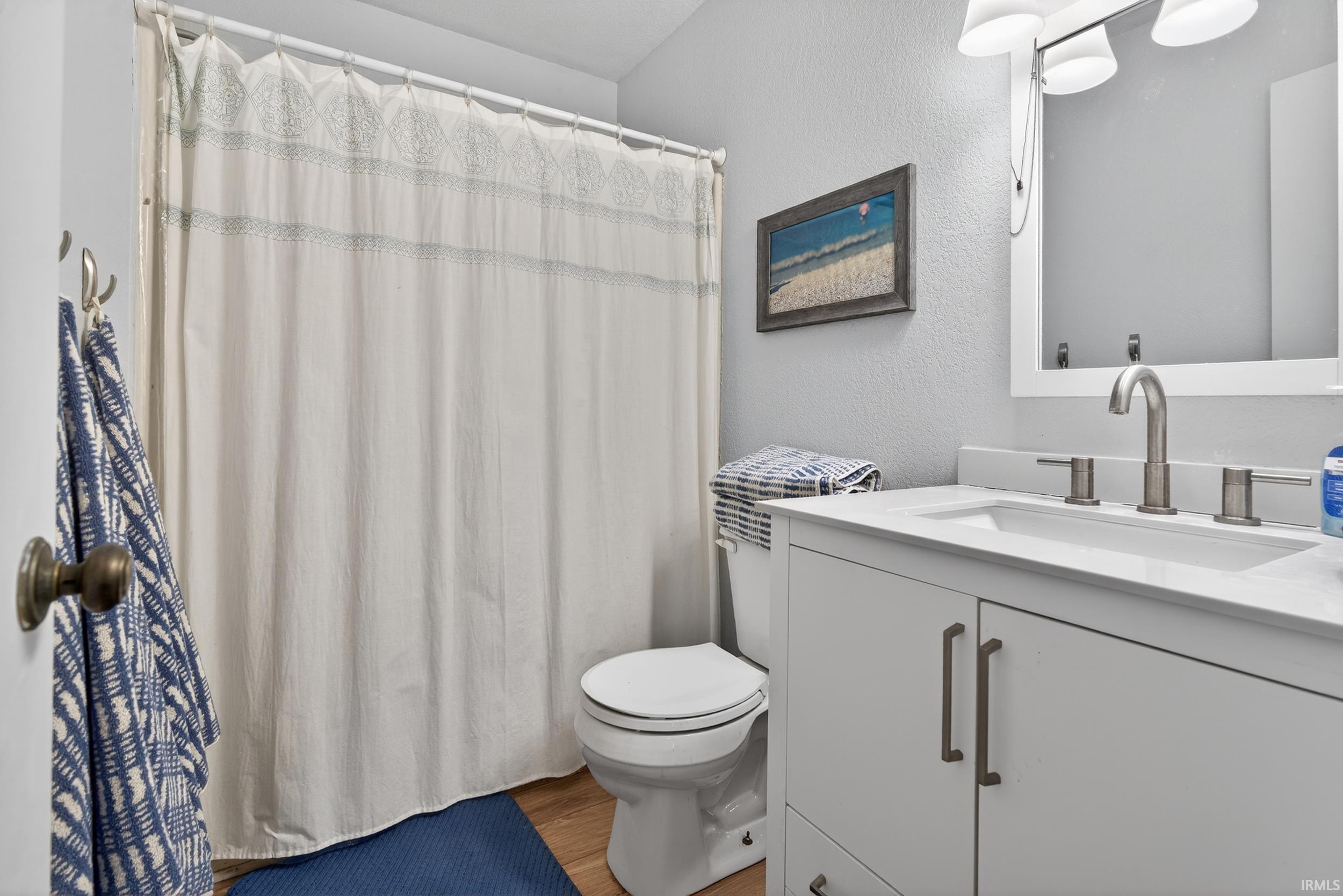 Full bath with vanity, a textured wall, a shower with curtain, and light wood-style floors
