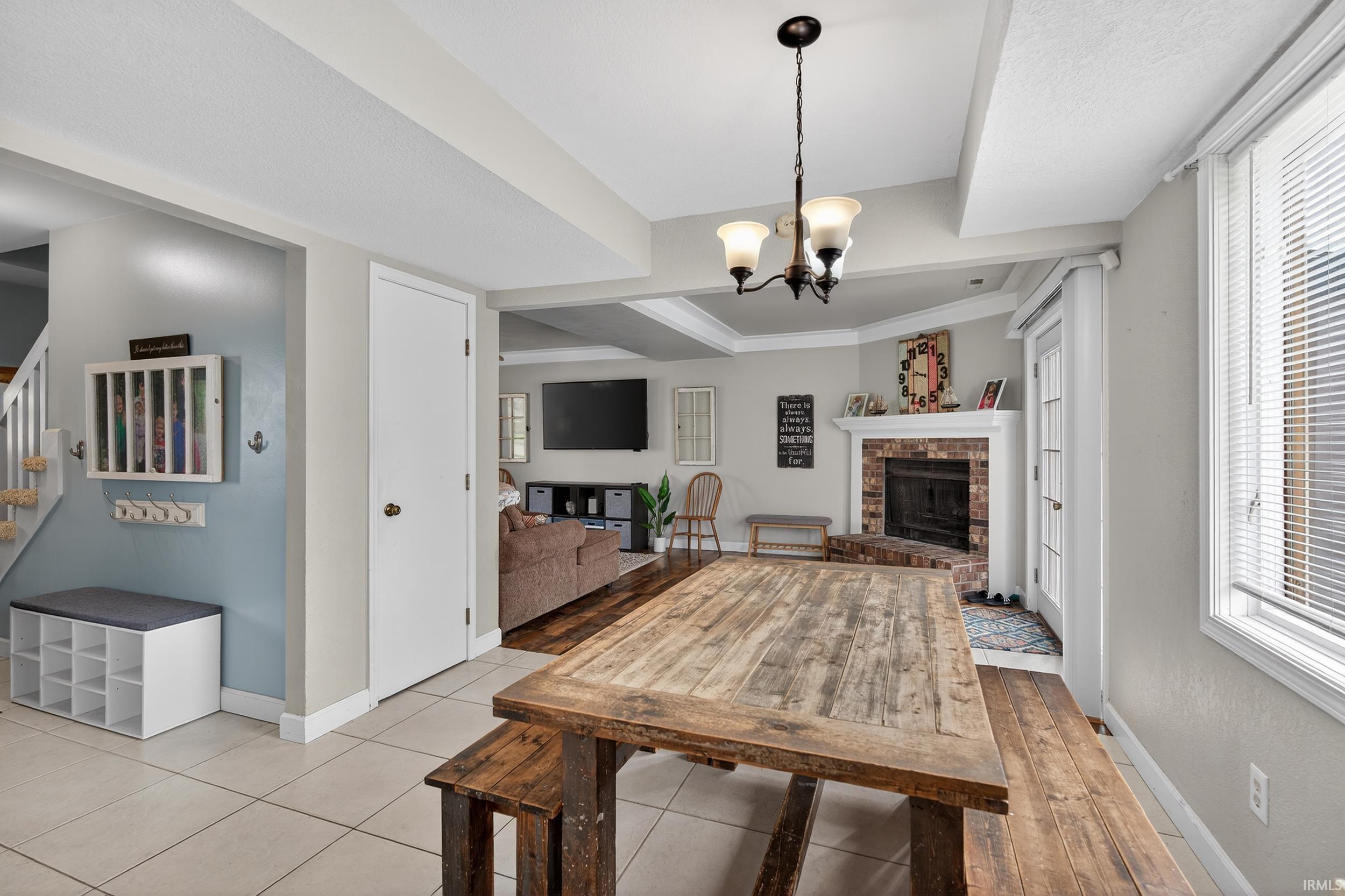 Dining area featuring a chandelier, healthy amount of natural light, a raised ceiling, light tile patterned flooring, and a fireplace