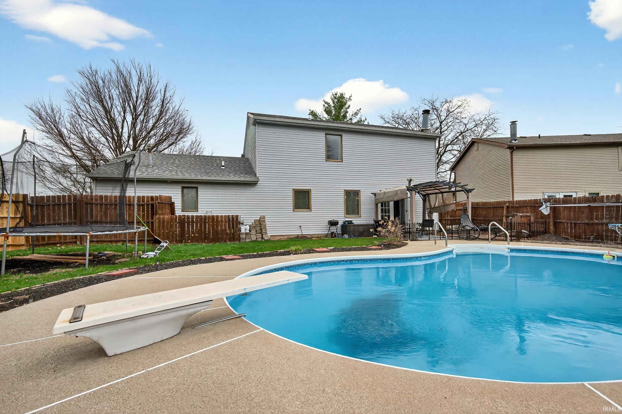 Back of property with a fenced backyard, a patio, a trampoline, a pergola, and roof with shingles