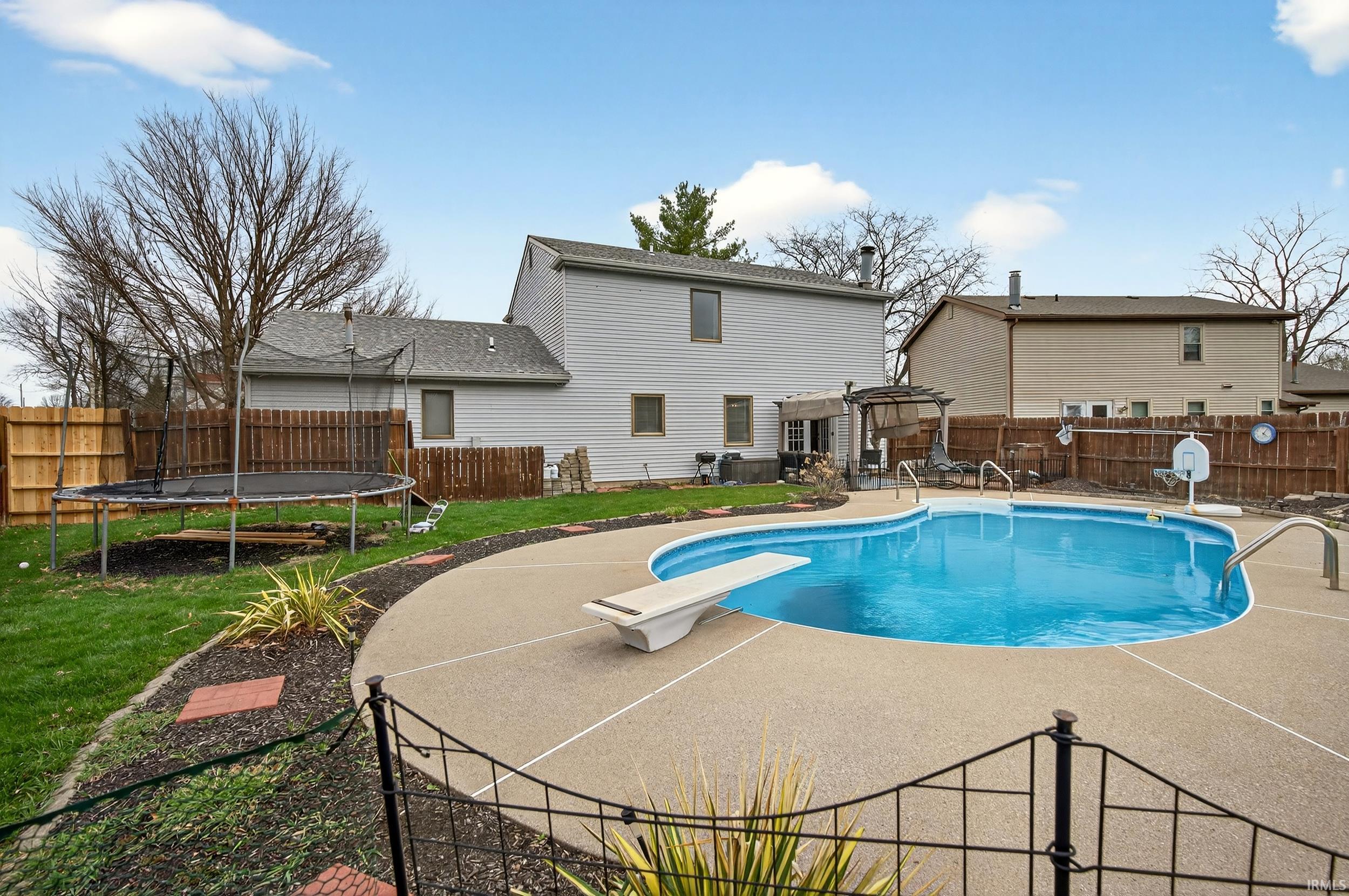 View of swimming pool featuring a trampoline, patio surround, a fenced backyard, and a diving board