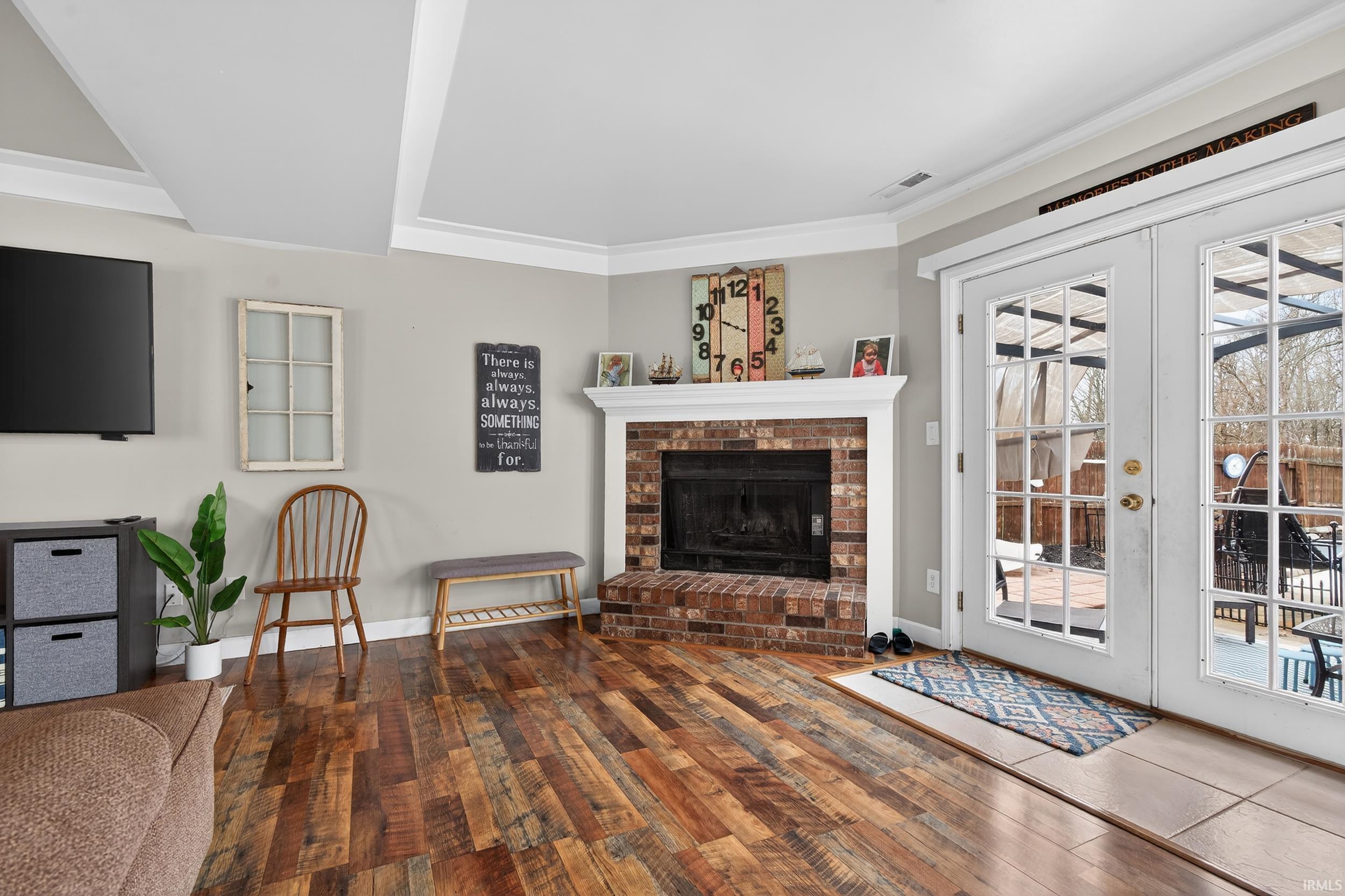Living area with hardwood / wood-style flooring, a brick fireplace, french doors, and crown molding