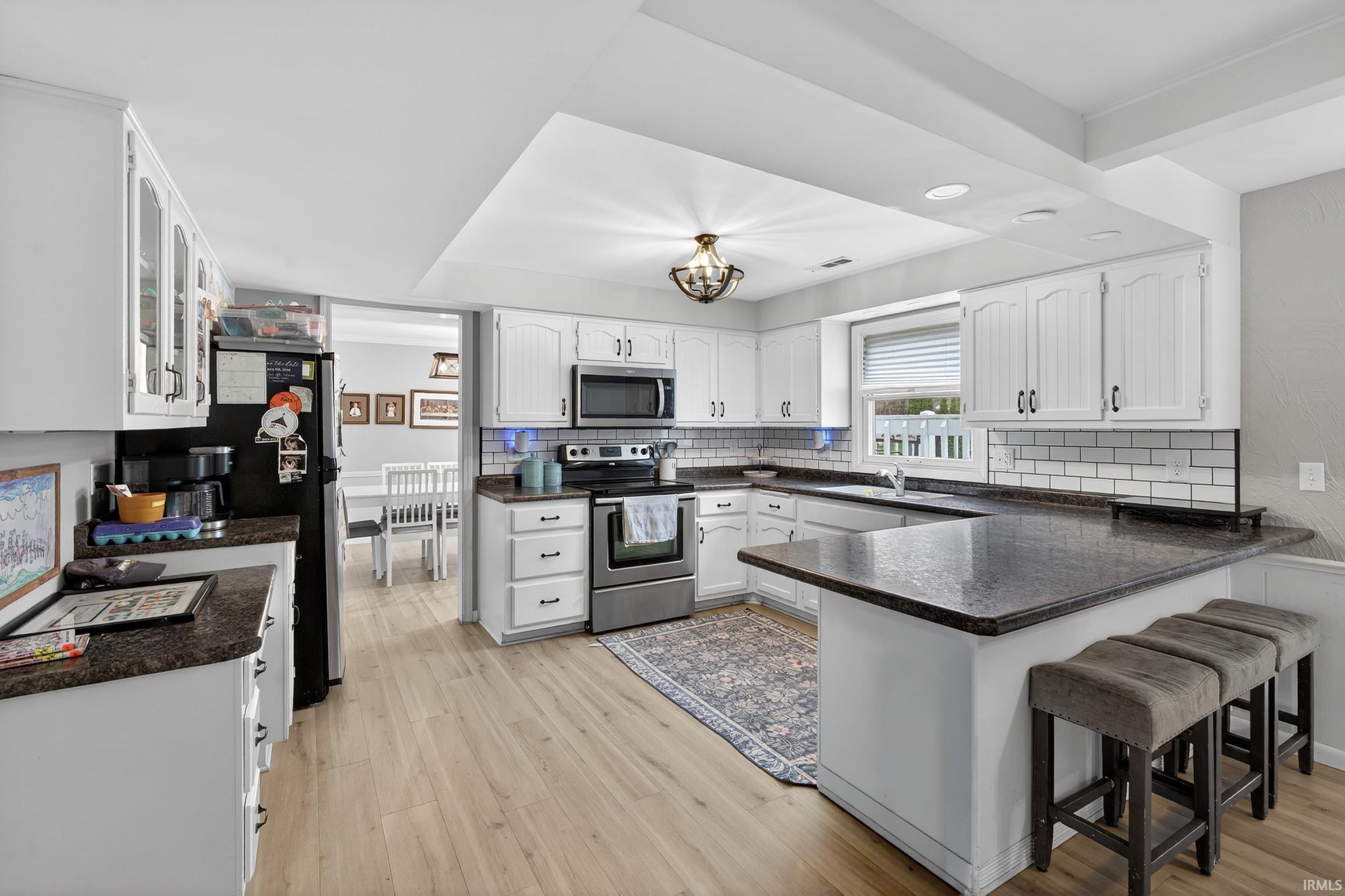 Kitchen featuring a peninsula, stainless steel appliances, white cabinetry, light wood-type flooring, and a breakfast bar