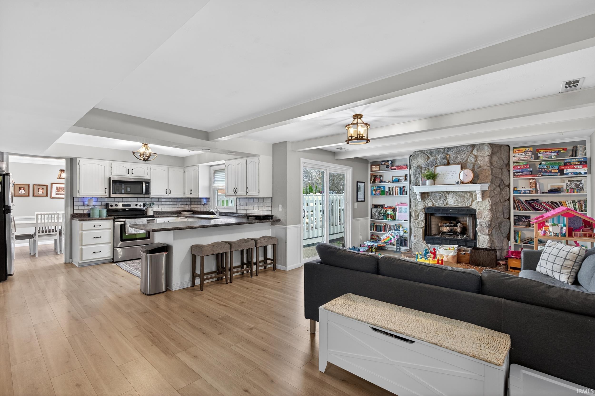 Living room with suspended lighting, light wood-type flooring, and a fireplace