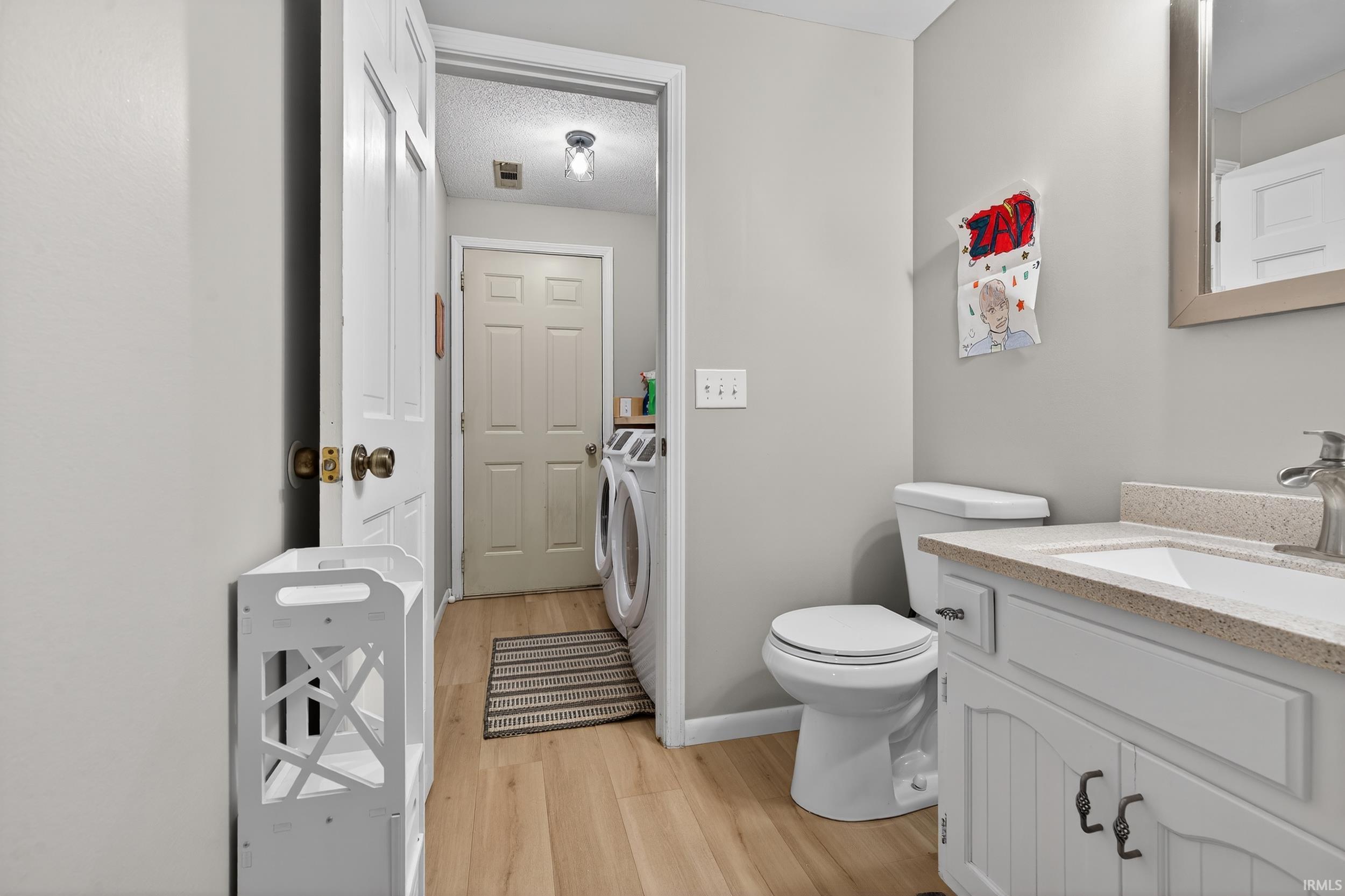 Half bath featuring vanity, washing machine and clothes dryer, light wood-type flooring, and a textured ceiling