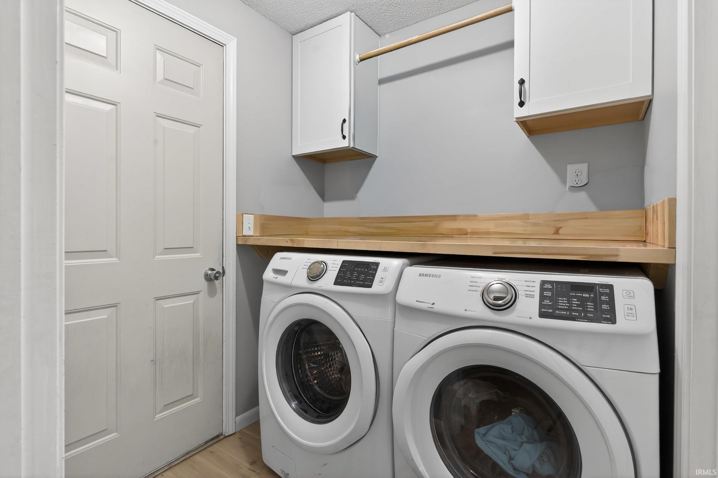 Laundry area featuring washing machine and clothes dryer, light wood-style flooring, a textured ceiling, and cabinet space