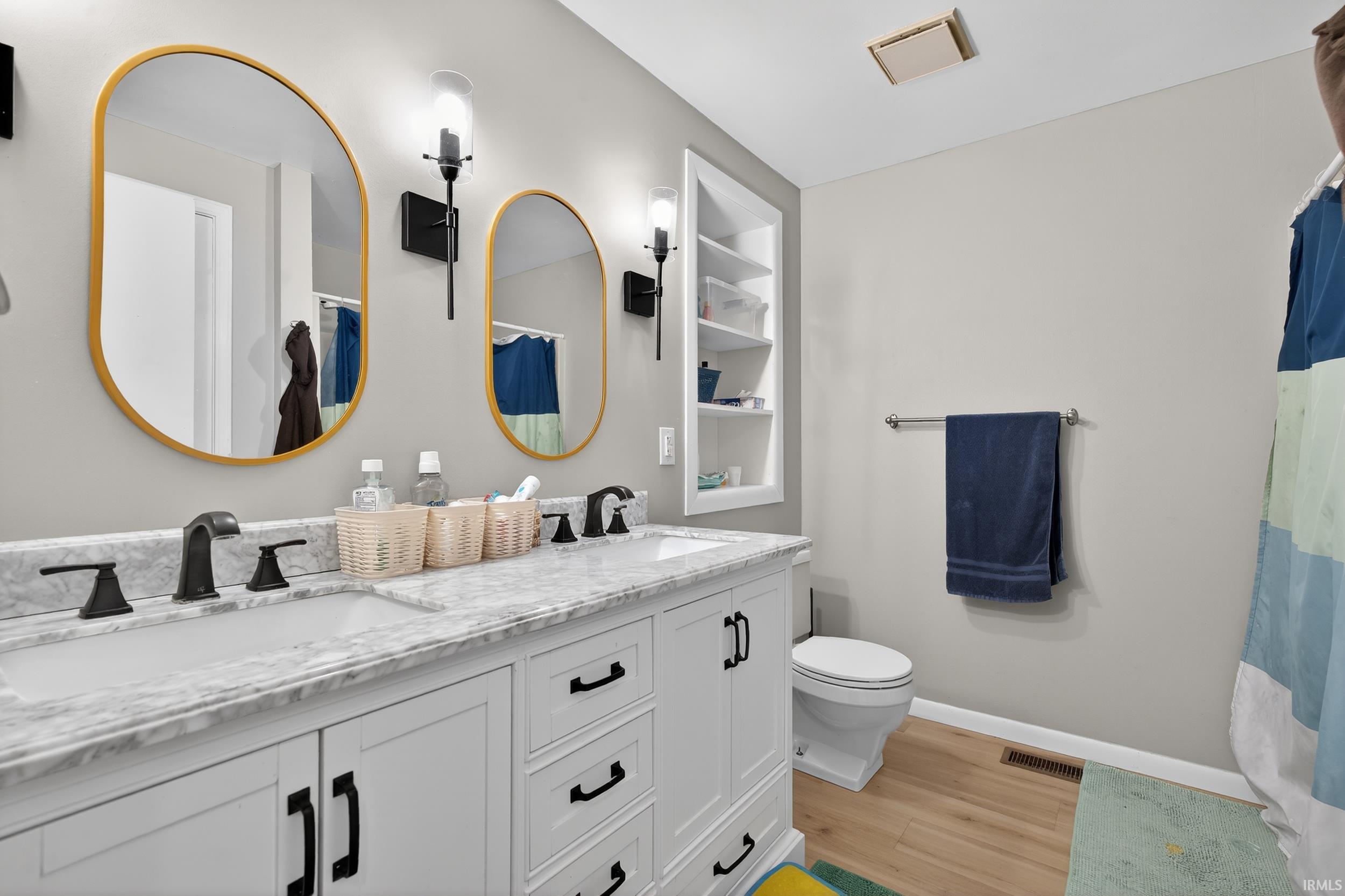 Full bath with double vanity, light wood-type flooring, and curtained shower
