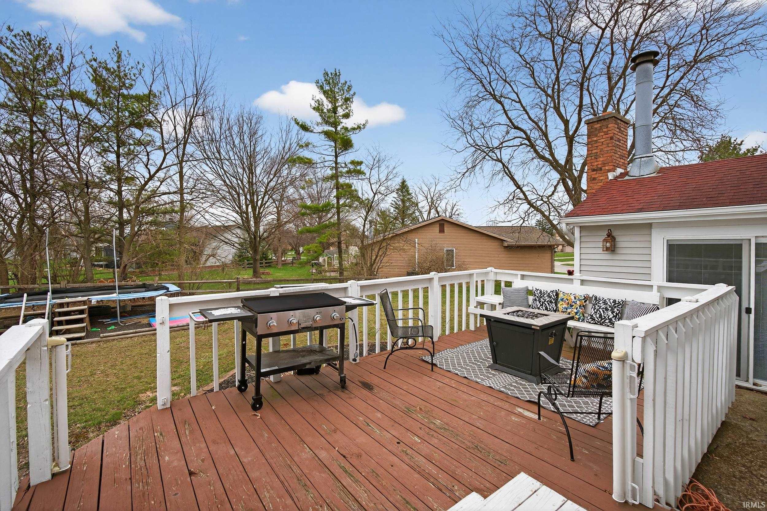 Wooden terrace with an outdoor fire pit, grilling area, a trampoline, and a lawn