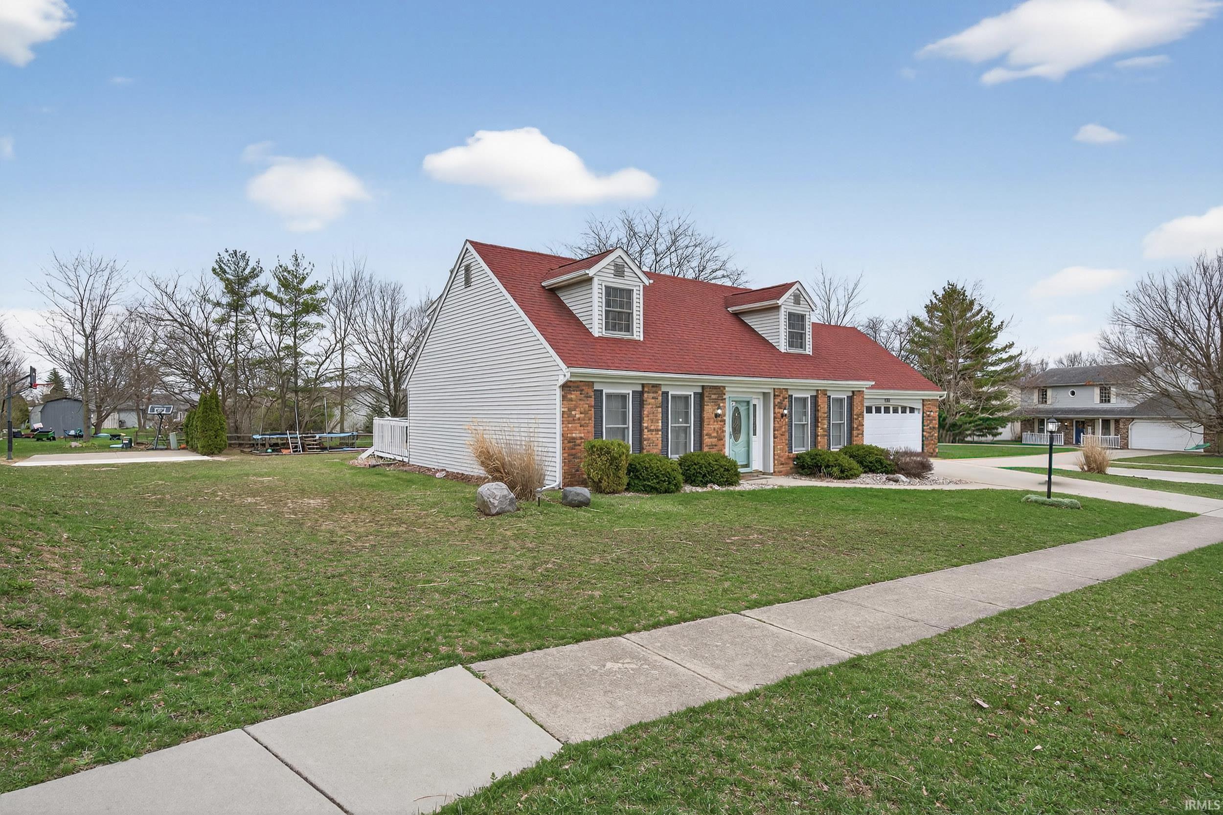 New england style home with a front lawn, brick siding, an attached garage, and concrete driveway