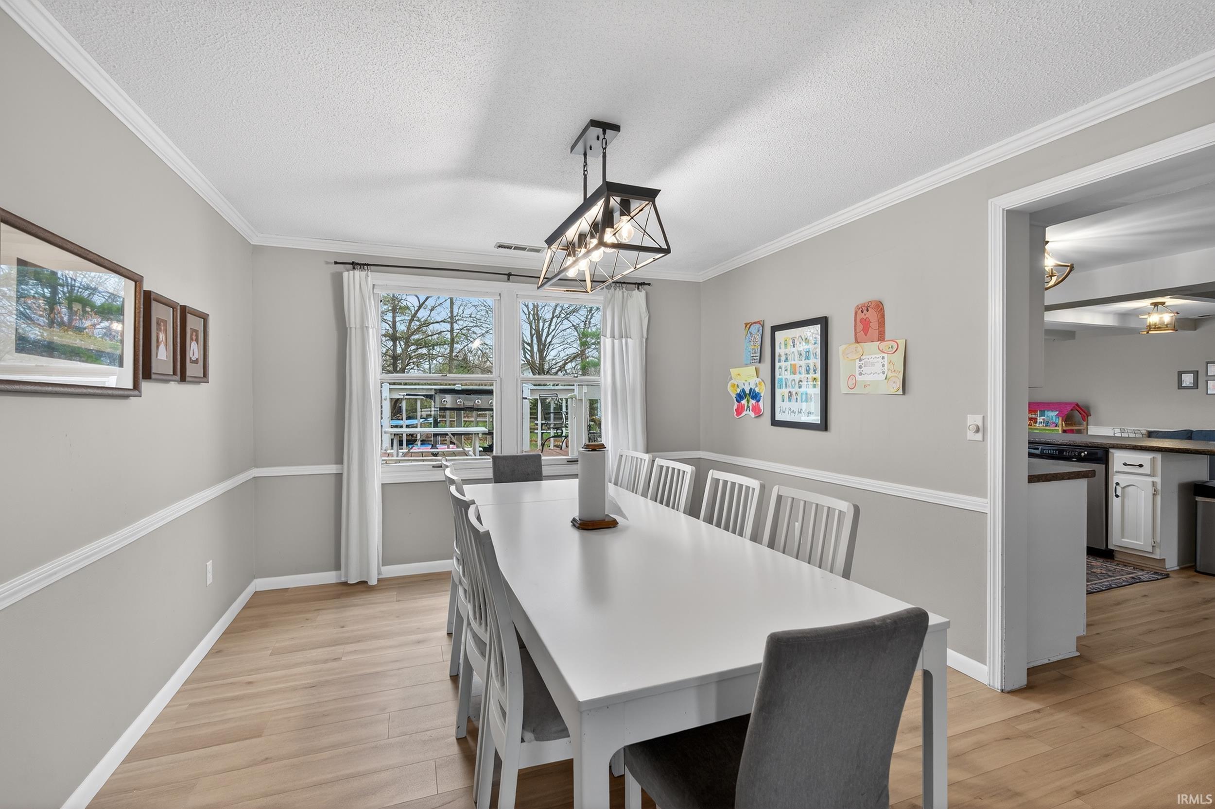 Dining room featuring light wood-style flooring, hanging lights, a textured ceiling, and crown molding