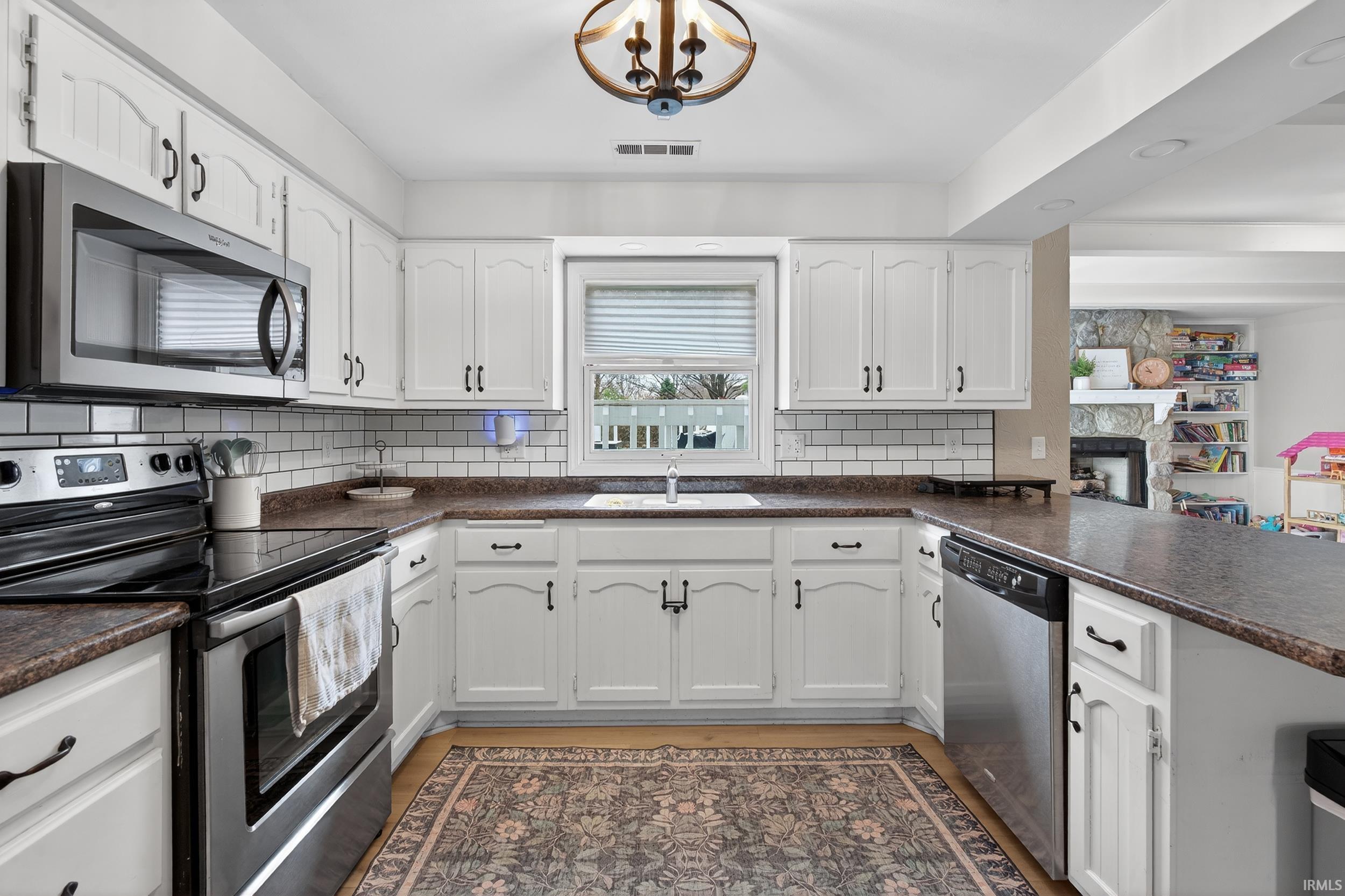 Kitchen featuring stainless steel appliances, dark countertops, white cabinets, and a stone fireplace
