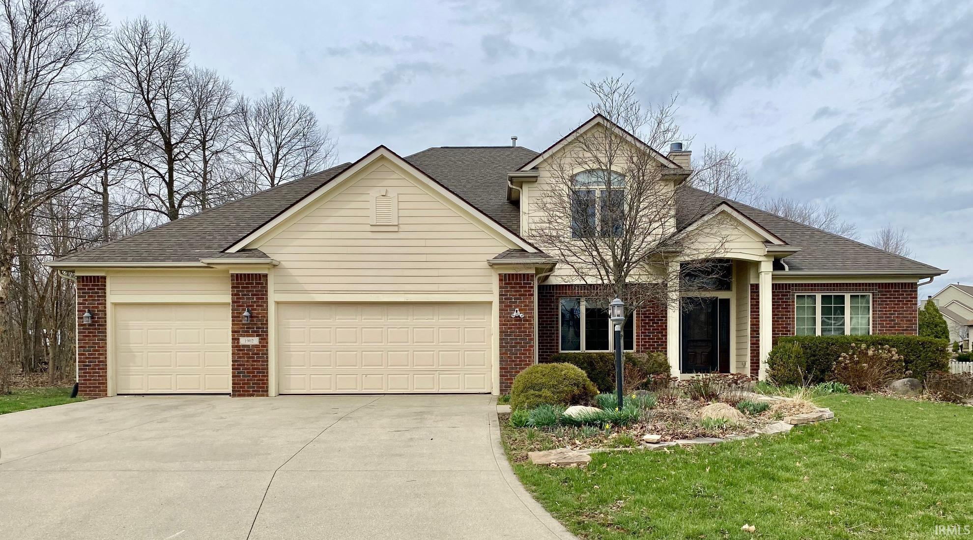 Traditional home with a garage, a shingled roof, driveway, and brick siding