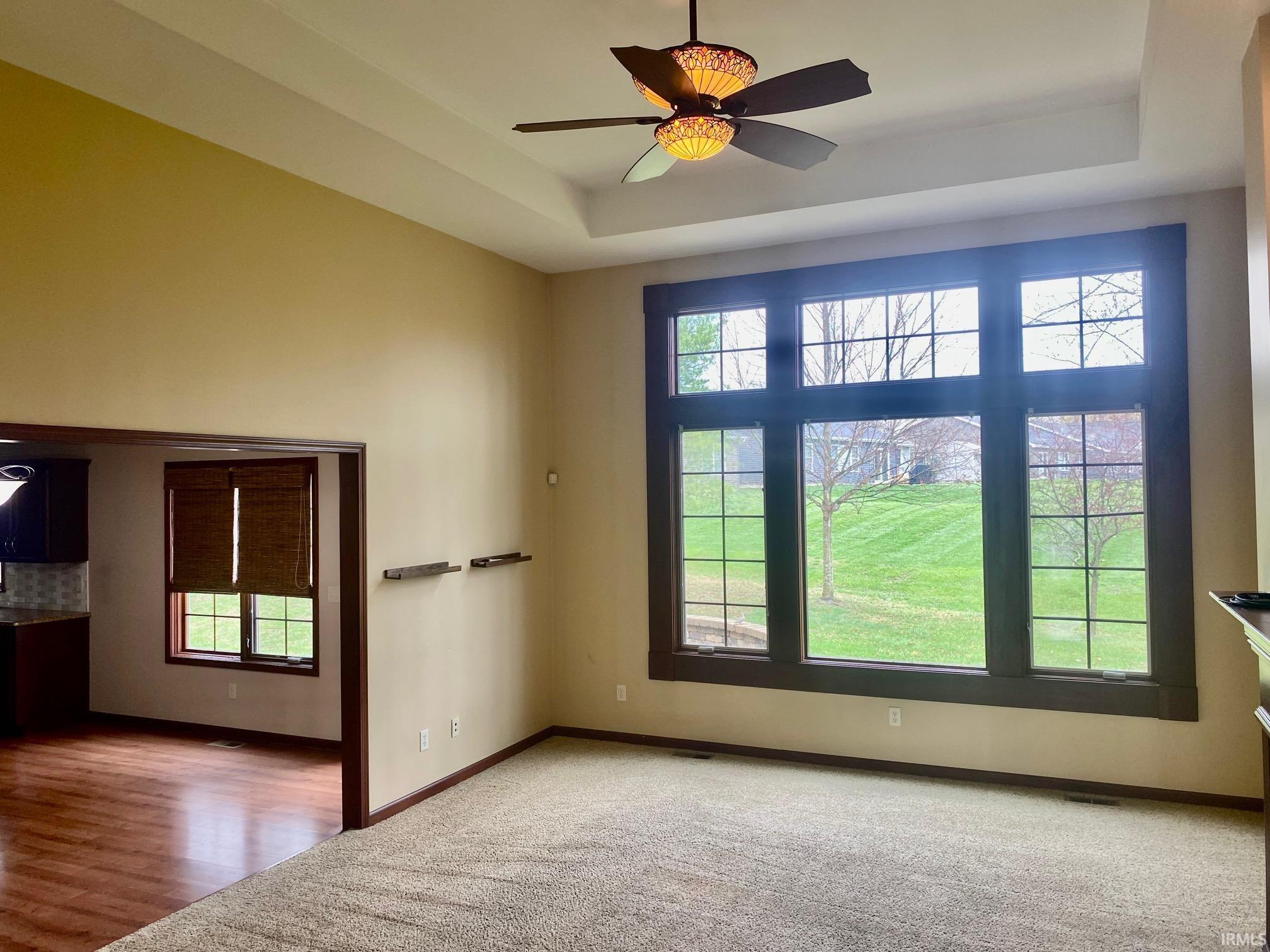 Unfurnished room featuring a ceiling fan, light colored carpet, and a tray ceiling