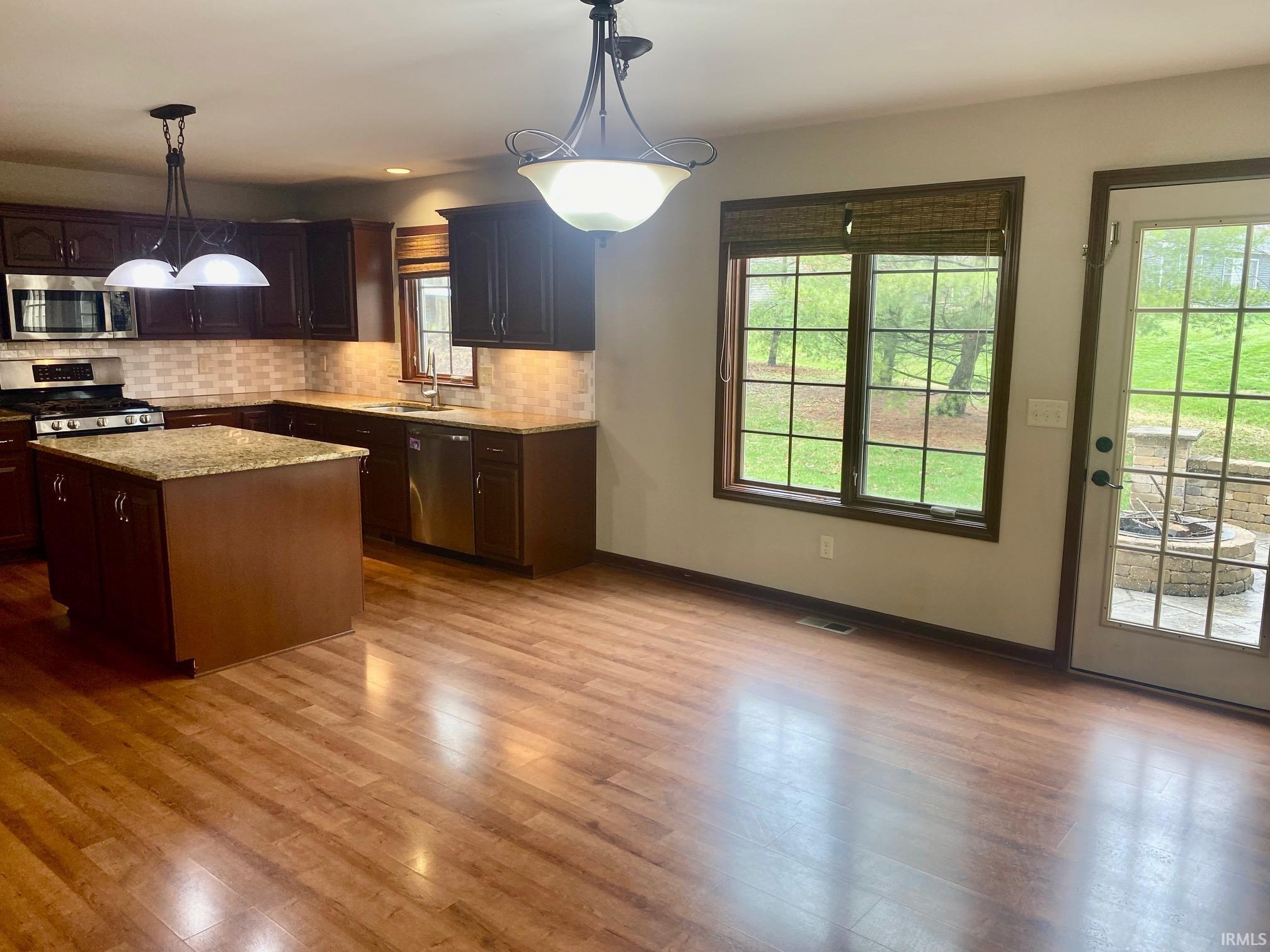 Kitchen with pendant lighting, stainless steel appliances, backsplash, a kitchen island, and light stone counters