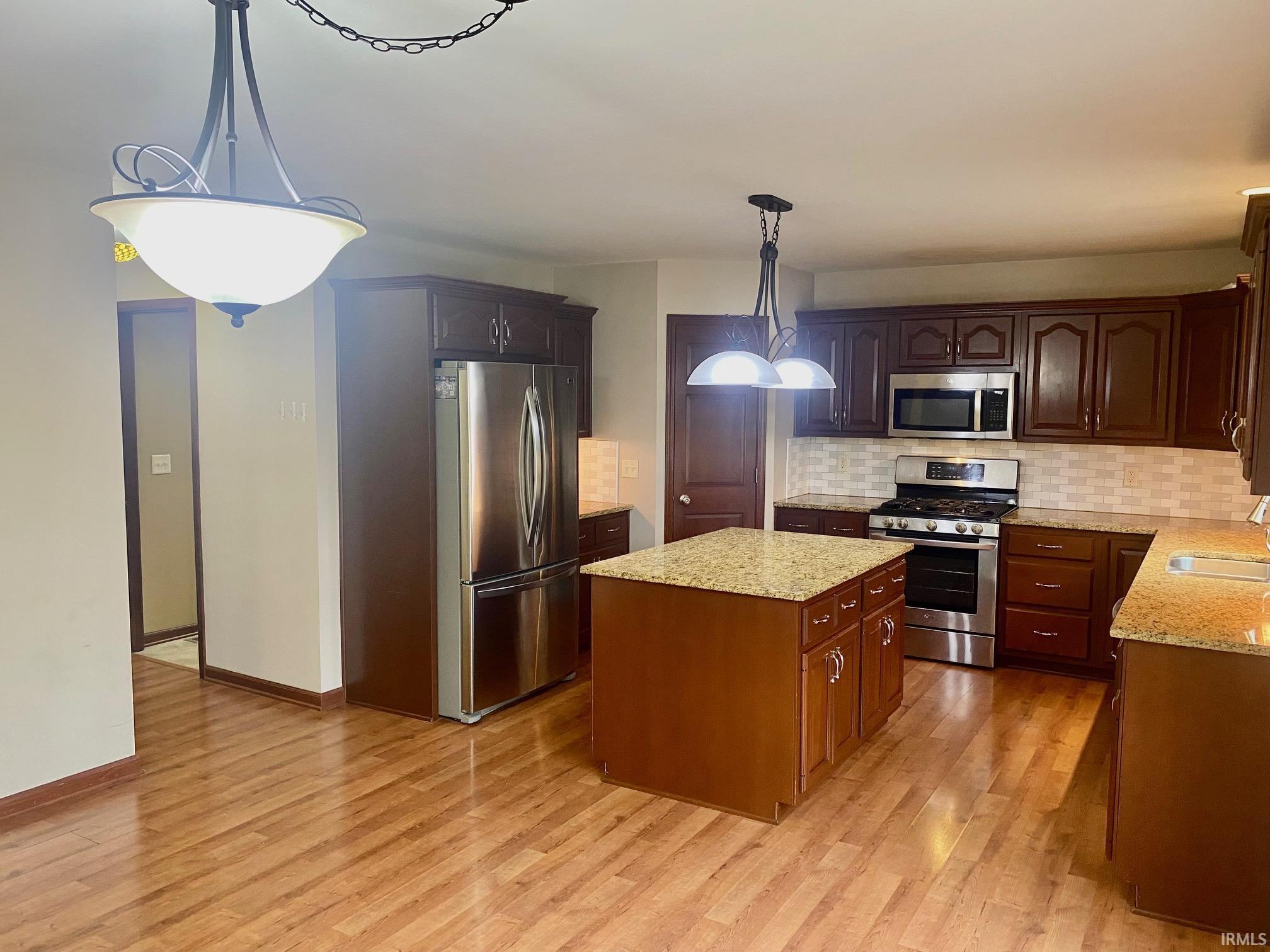 Kitchen with stainless steel appliances, a center island, tasteful backsplash, light stone counters, and light wood finished floors