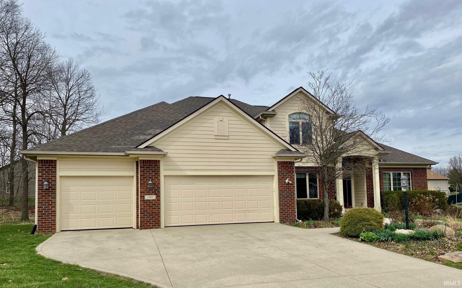 Traditional home featuring brick siding, a garage, concrete driveway, and a shingled roof